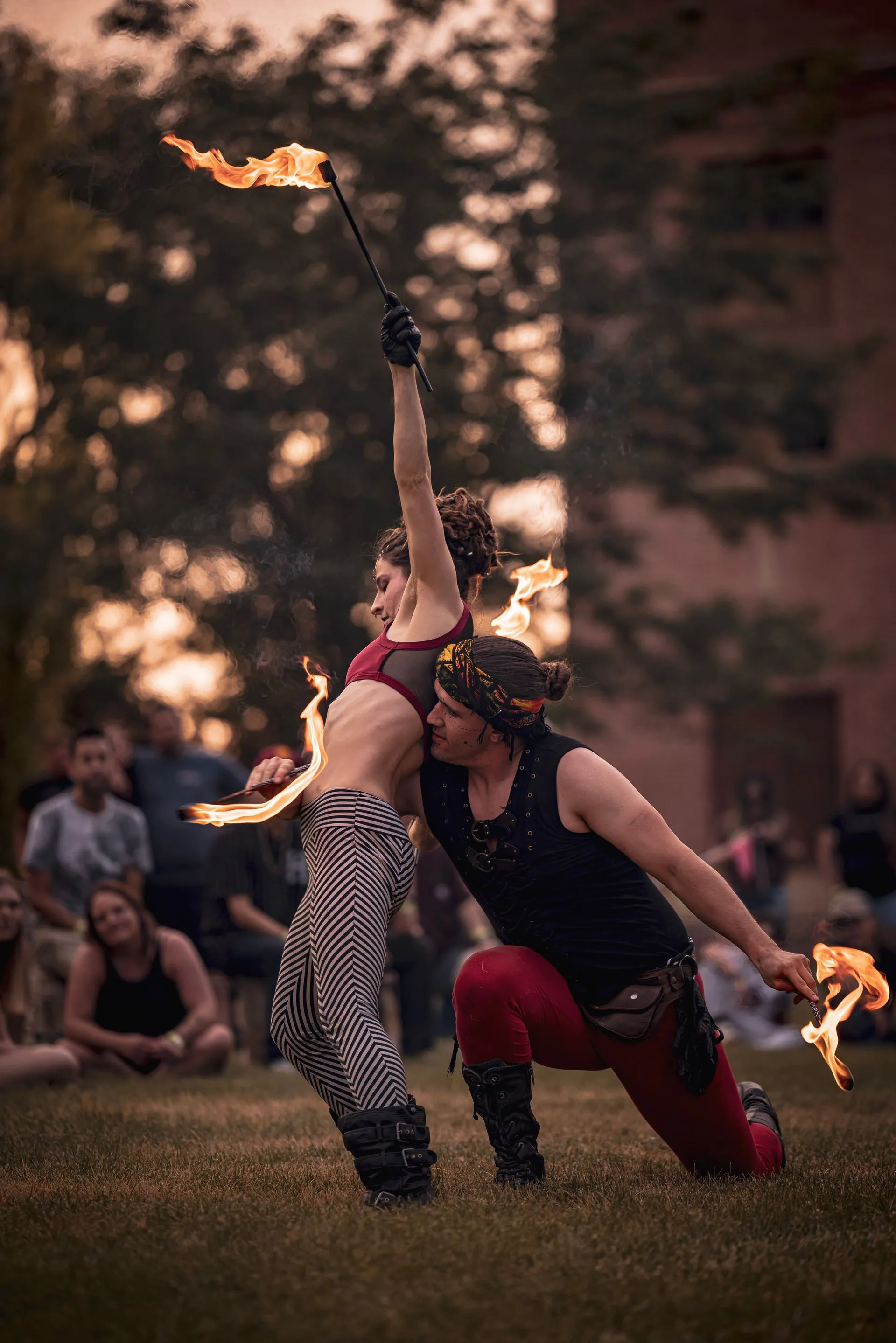 A man and a woman are performing a fire show in a park.