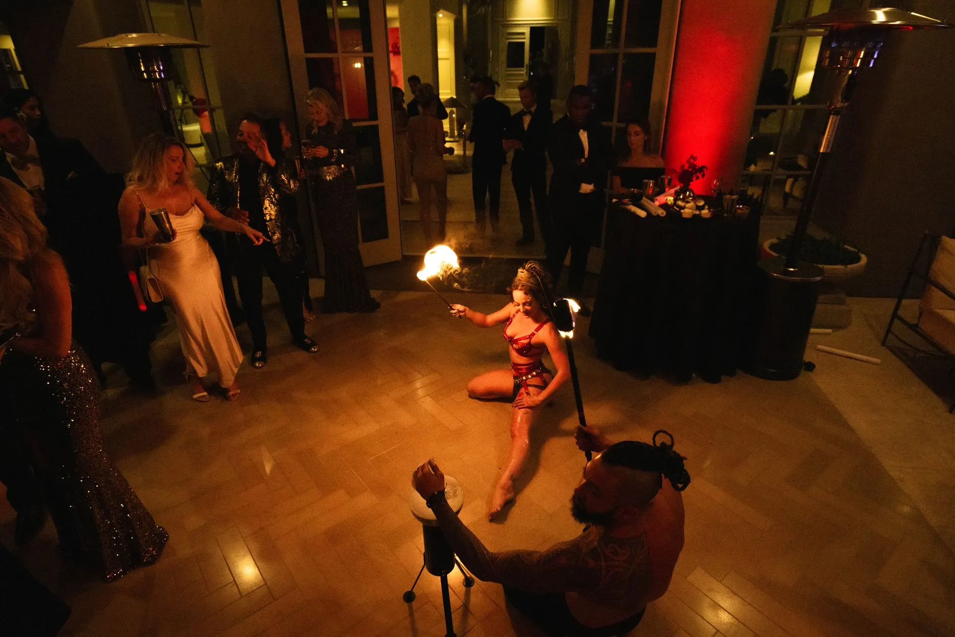 A man is sitting on the floor holding a fire torch while a woman performs a fire show.