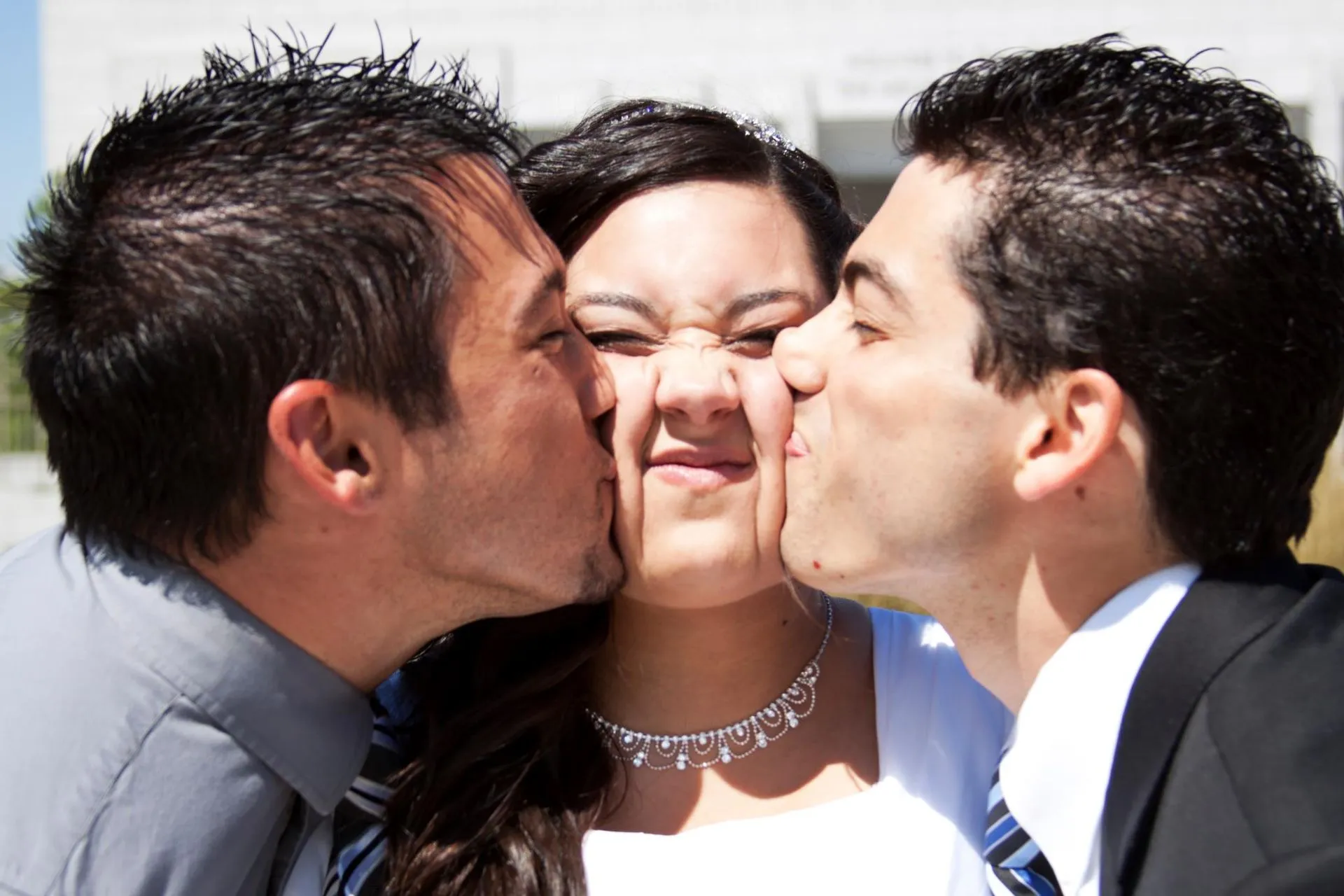 A couple of men kissing a woman on the cheek