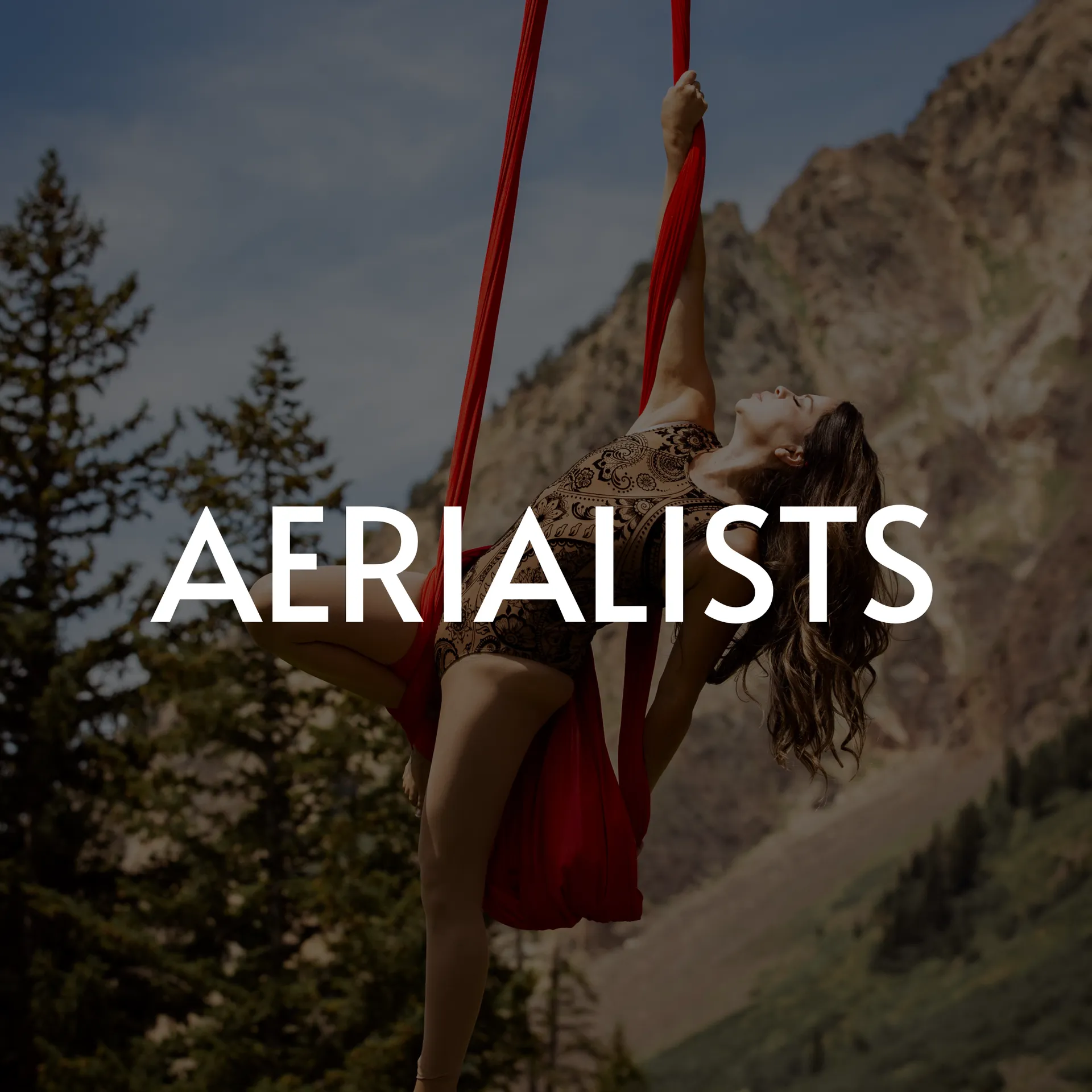 A performer doing an aerial silk routine outdoors against a mountain backdrop