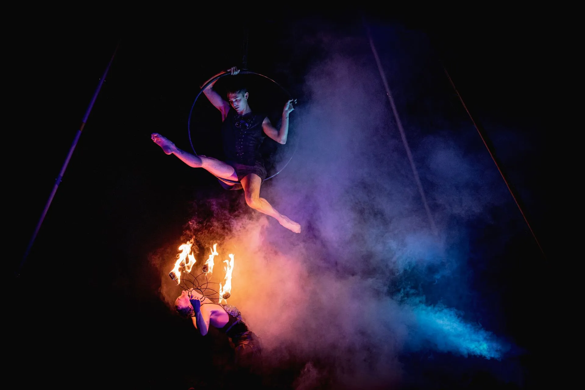 A woman is flying through the air in an aerial hoop with fire.