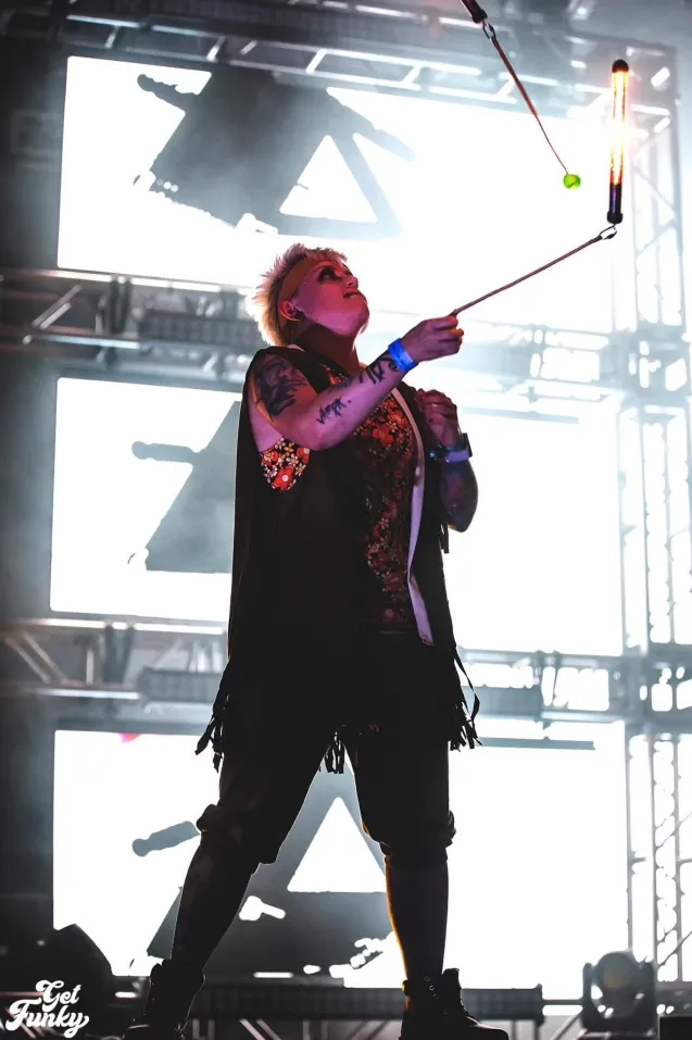 A man is juggling a torch on a stage while wearing a black vest