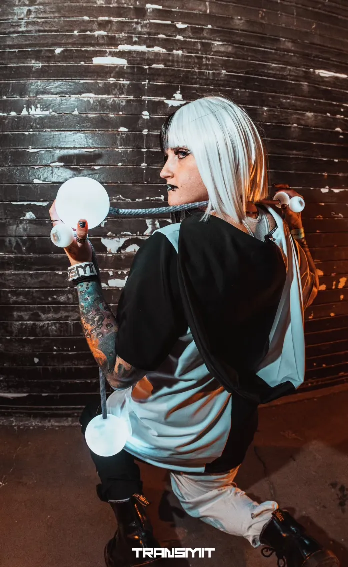 A woman with white hair is kneeling down in front of a brick wall holding a light bulb.