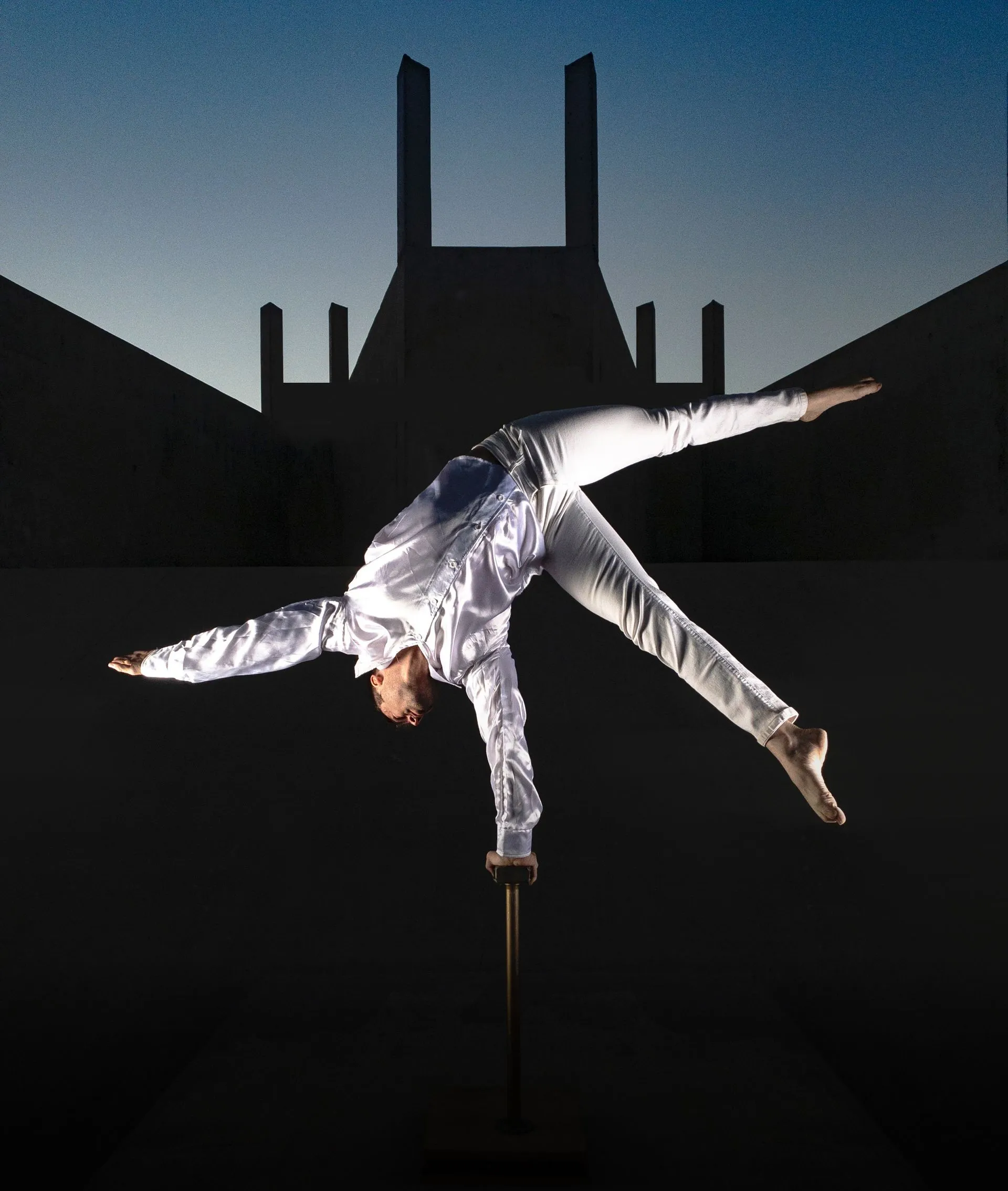 A man in a white shirt is doing a handstand in front of a building