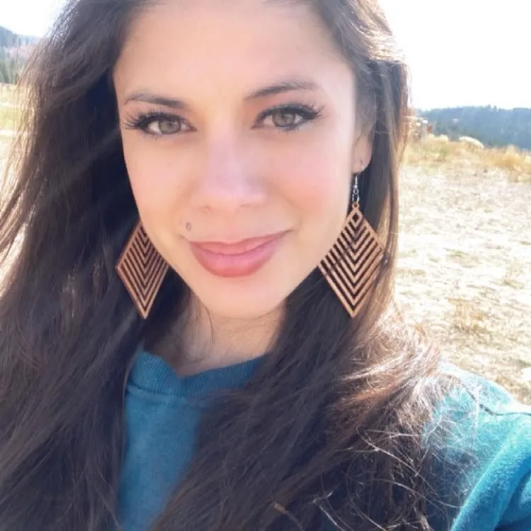 A woman wearing a blue shirt and diamond shaped earrings