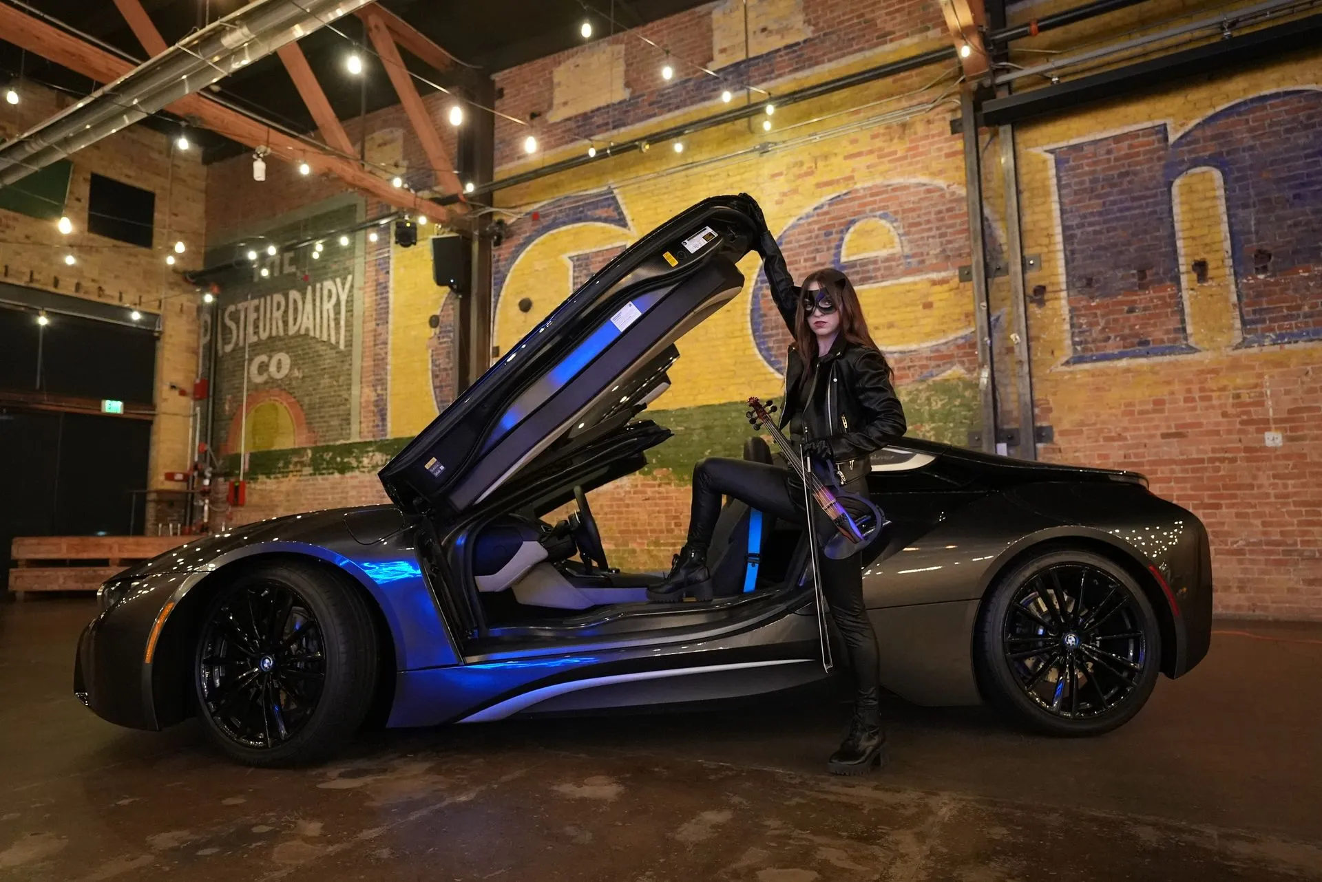 A woman is standing next to a blue sports car with the hood open.