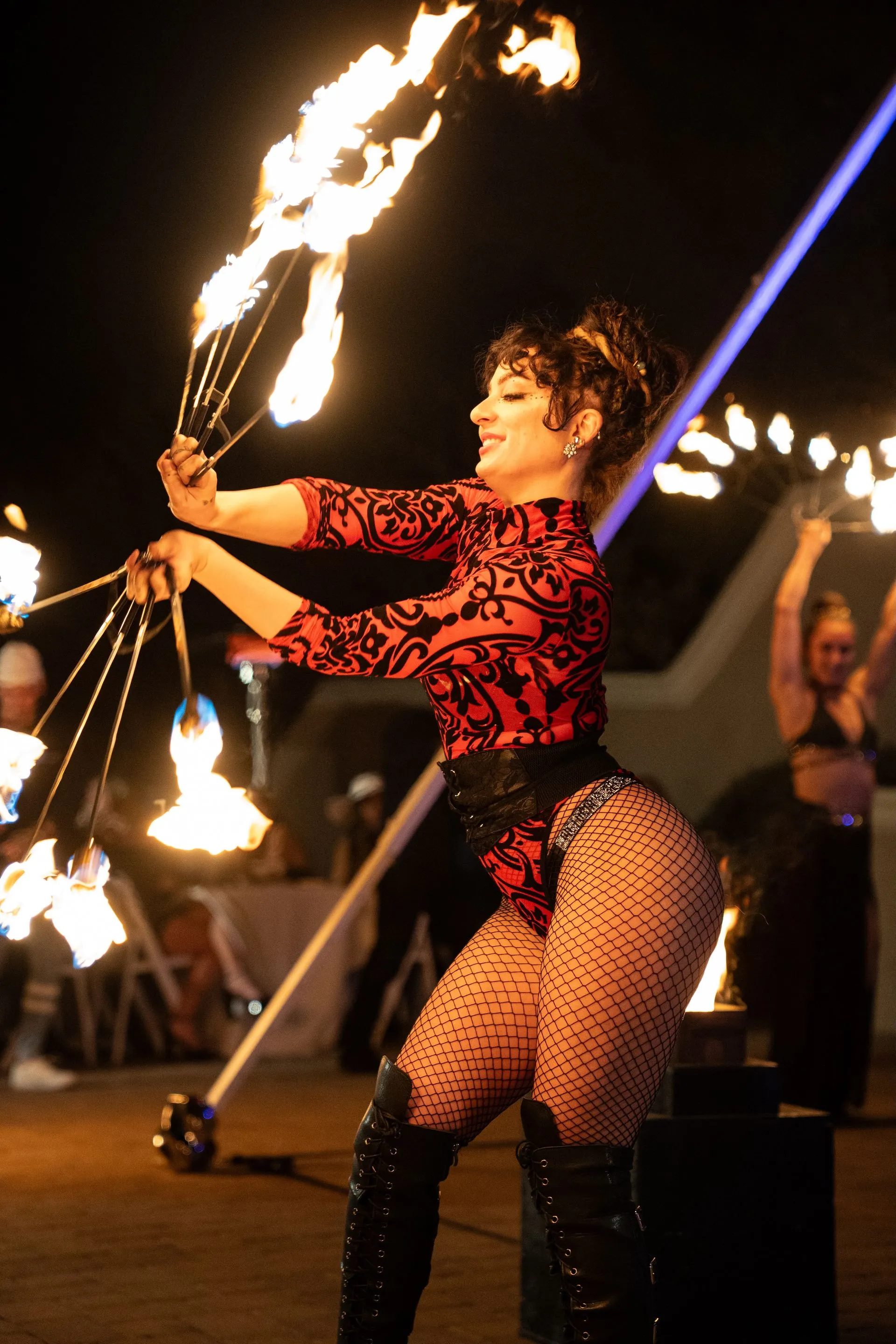 A woman in a red bodysuit is holding a bunch of fire sticks.