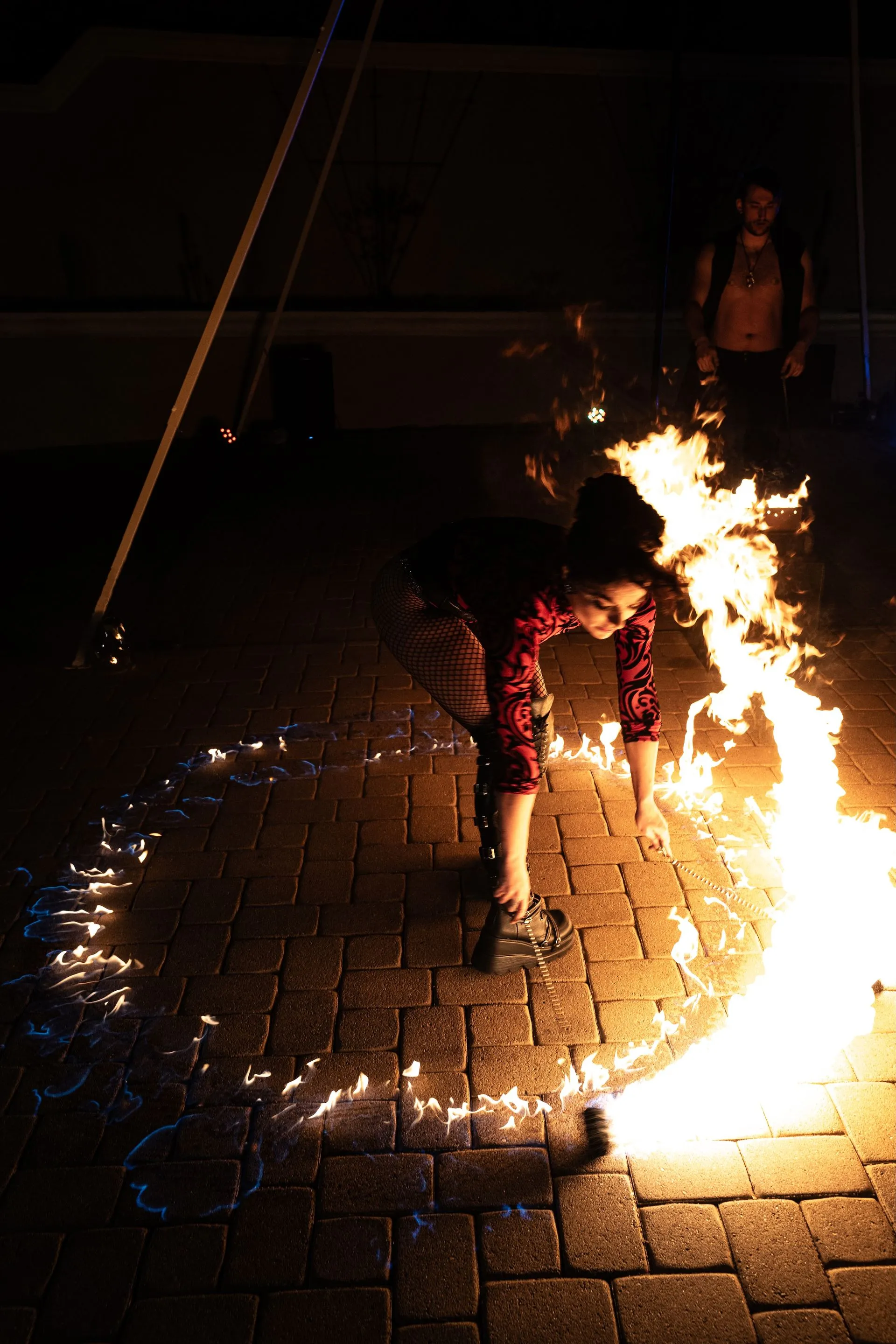 A person is playing with fire on a brick sidewalk at night.