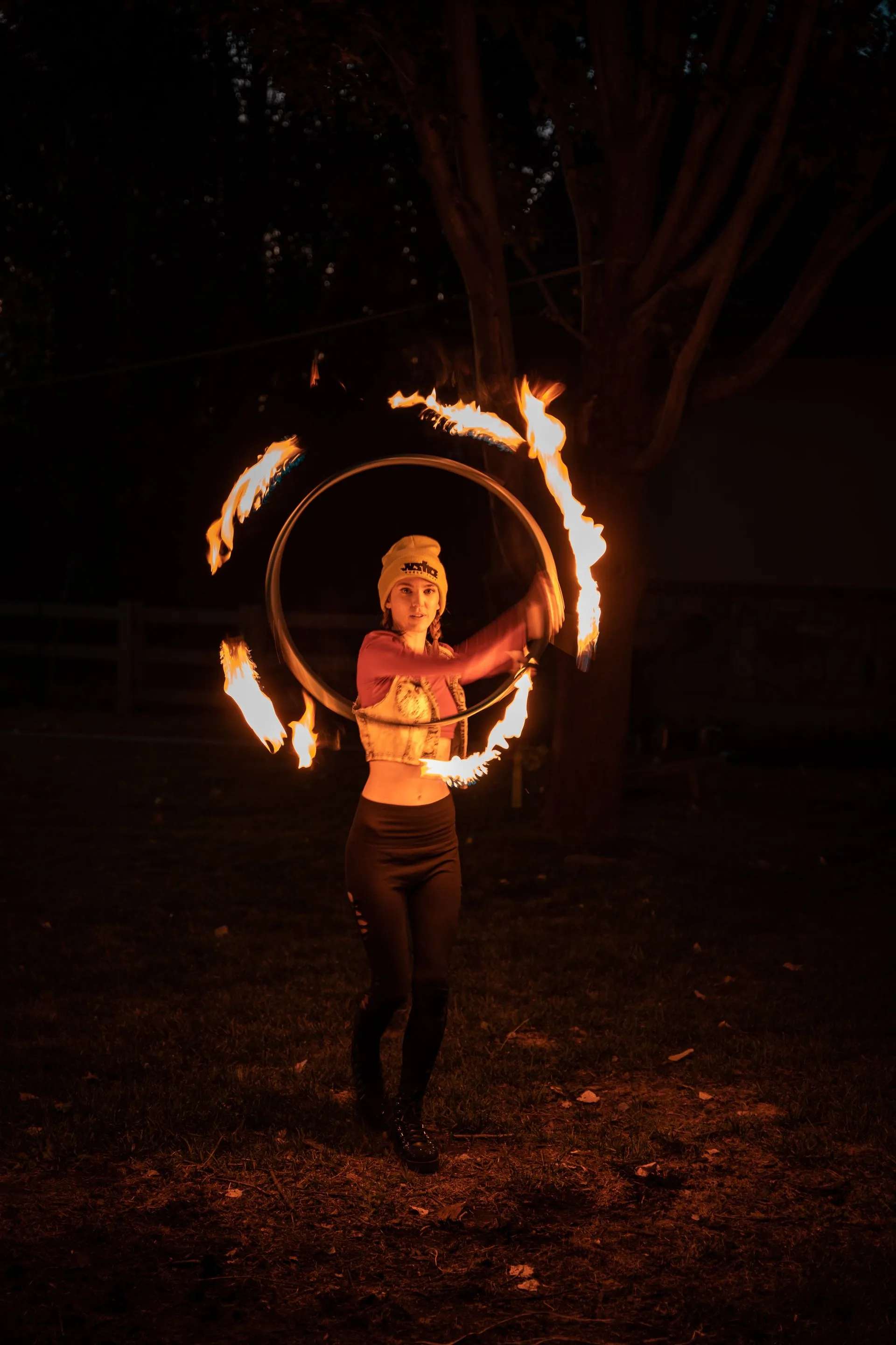 A woman is spinning a fire hoop in the dark.