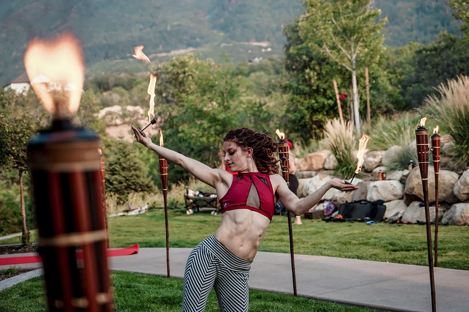 A woman is dancing with a fire torch in a park.
