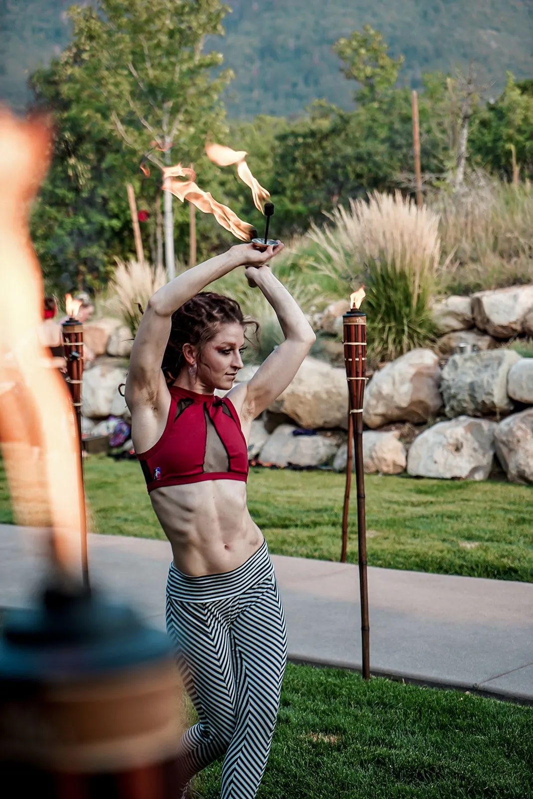 A woman is holding a torch over her head while dancing in a park.