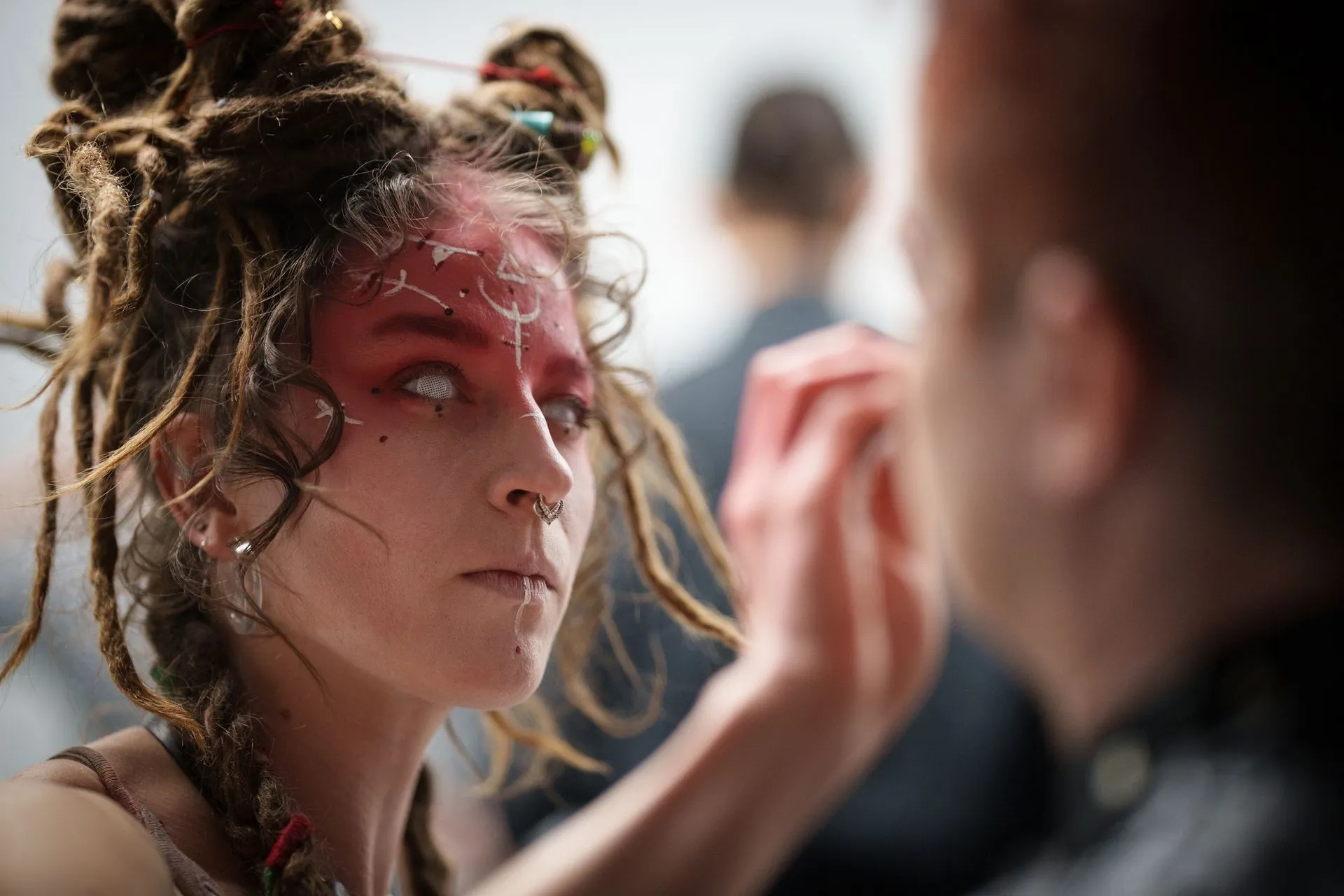 A woman with dreadlocks is getting her face painted by a man.