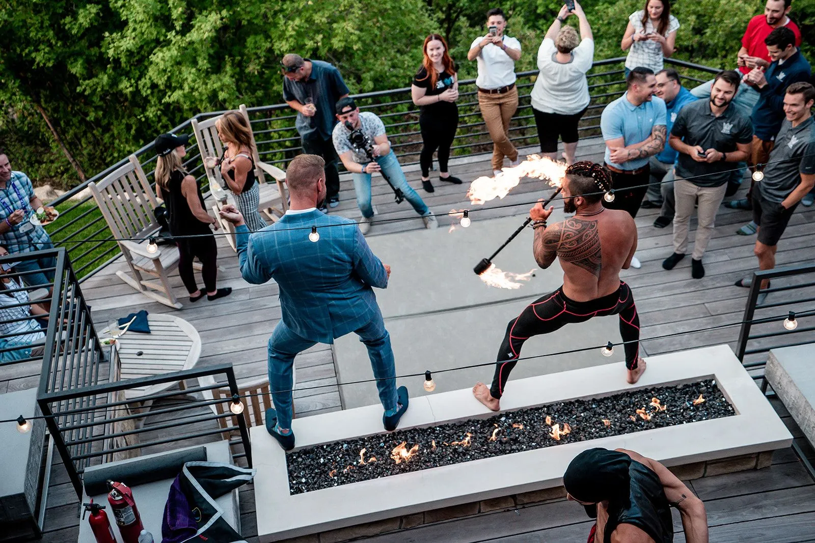 A group of people are standing around a fire pit on a deck.