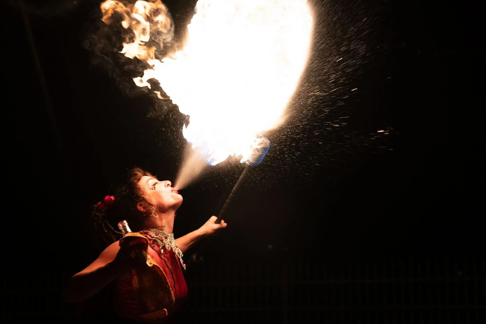 A woman is blowing fire from her mouth in the dark.