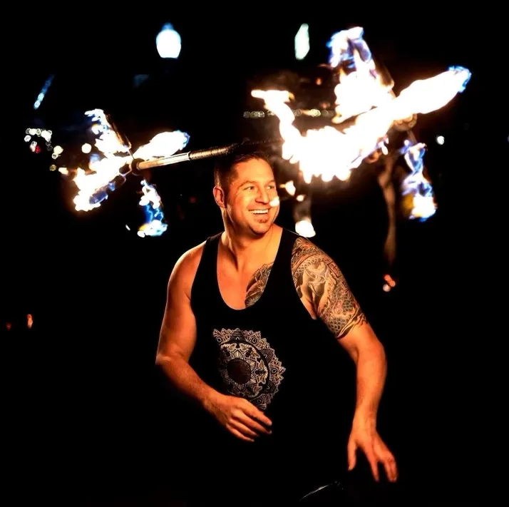 A man with a tattoo on his arm is holding a torch in the dark