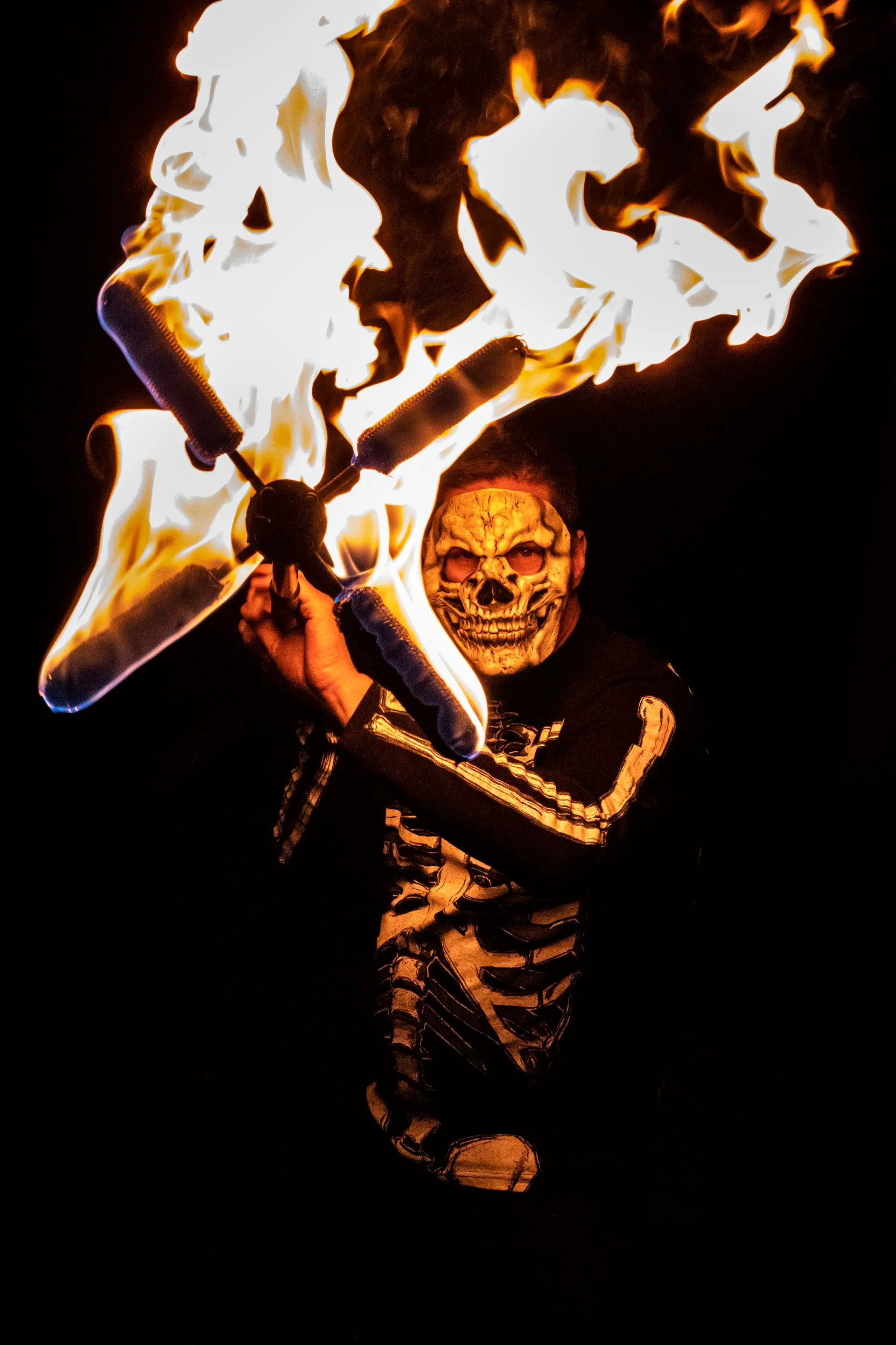 A man in a skeleton costume is holding a stick of fire.