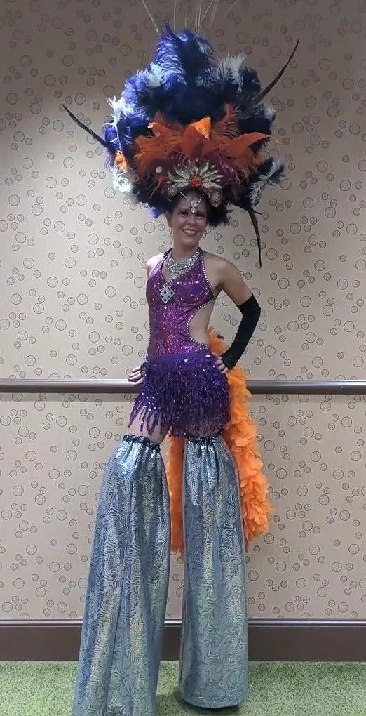 A woman in a carnival costume is standing on stilts.