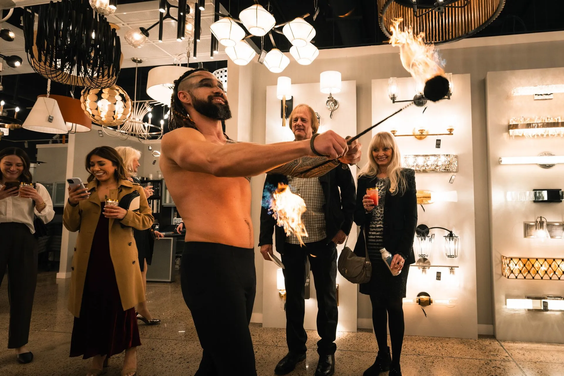 A shirtless man is holding a stick with flames coming out of it.