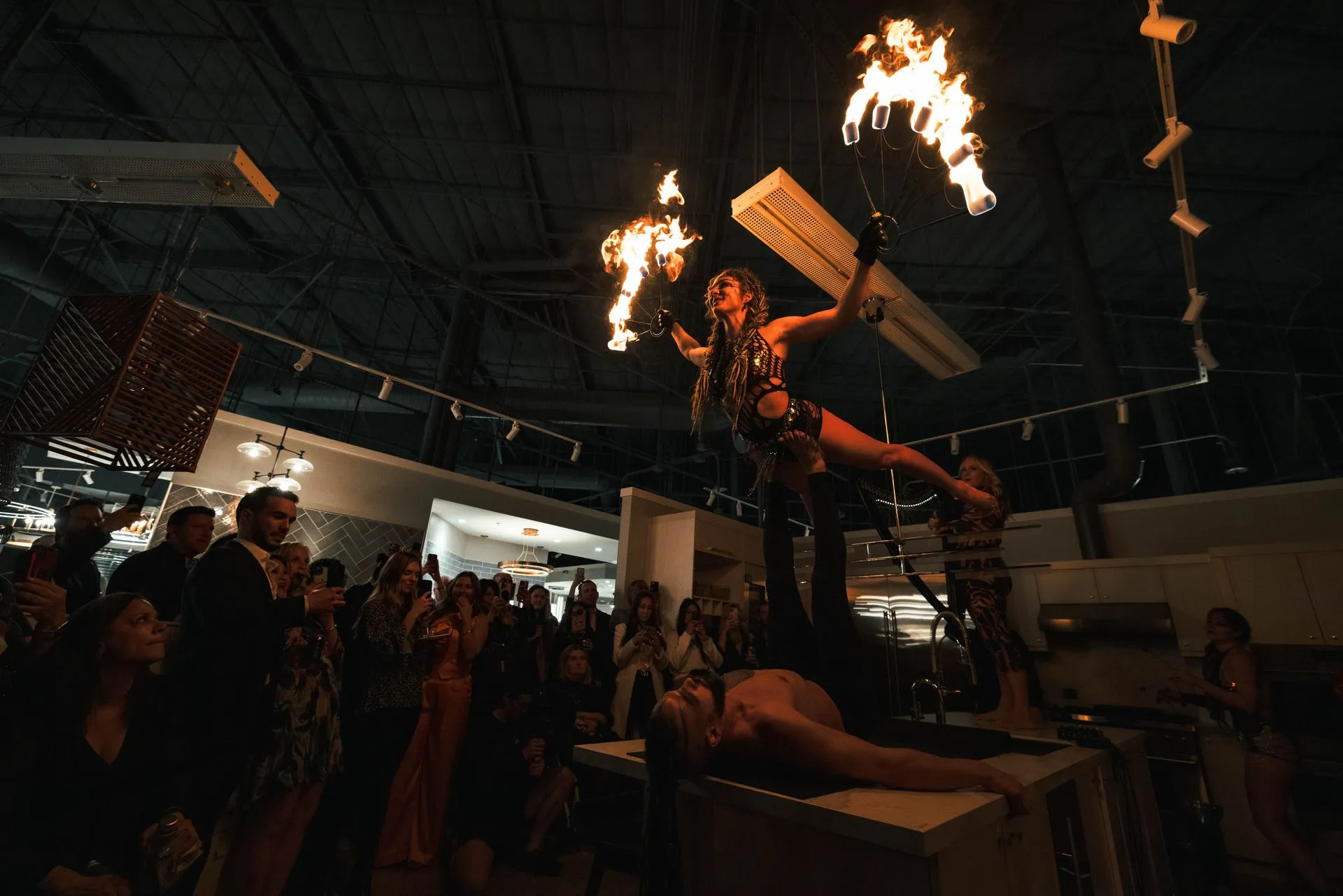 A group of people are watching a fire show in a dark room.