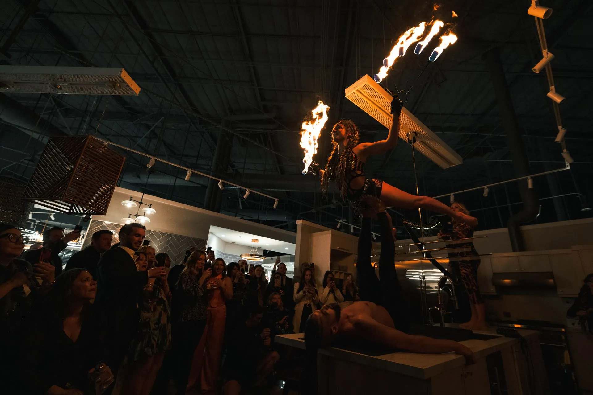 A group of people are watching a fire show in a dark room.