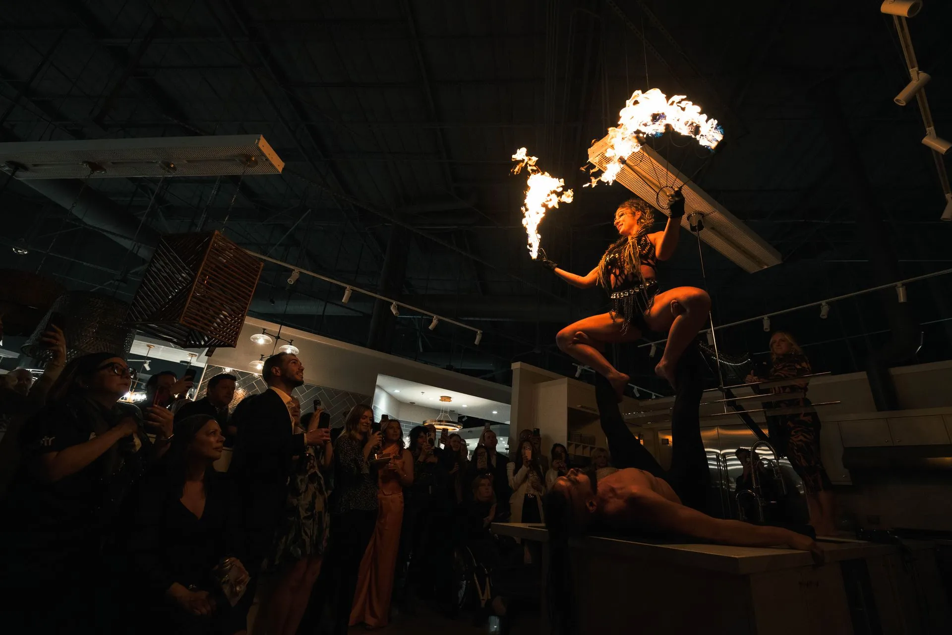 A man and woman performing acrobatic fire indoors up on a counter top.