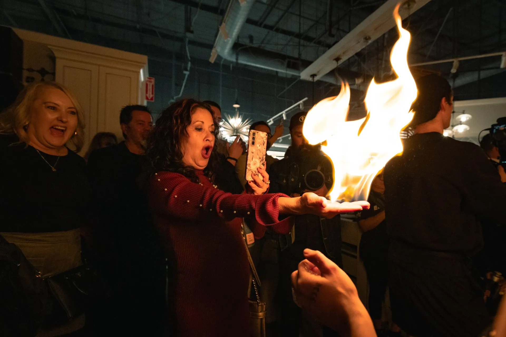 A woman is taking a picture of a fire with her phone.