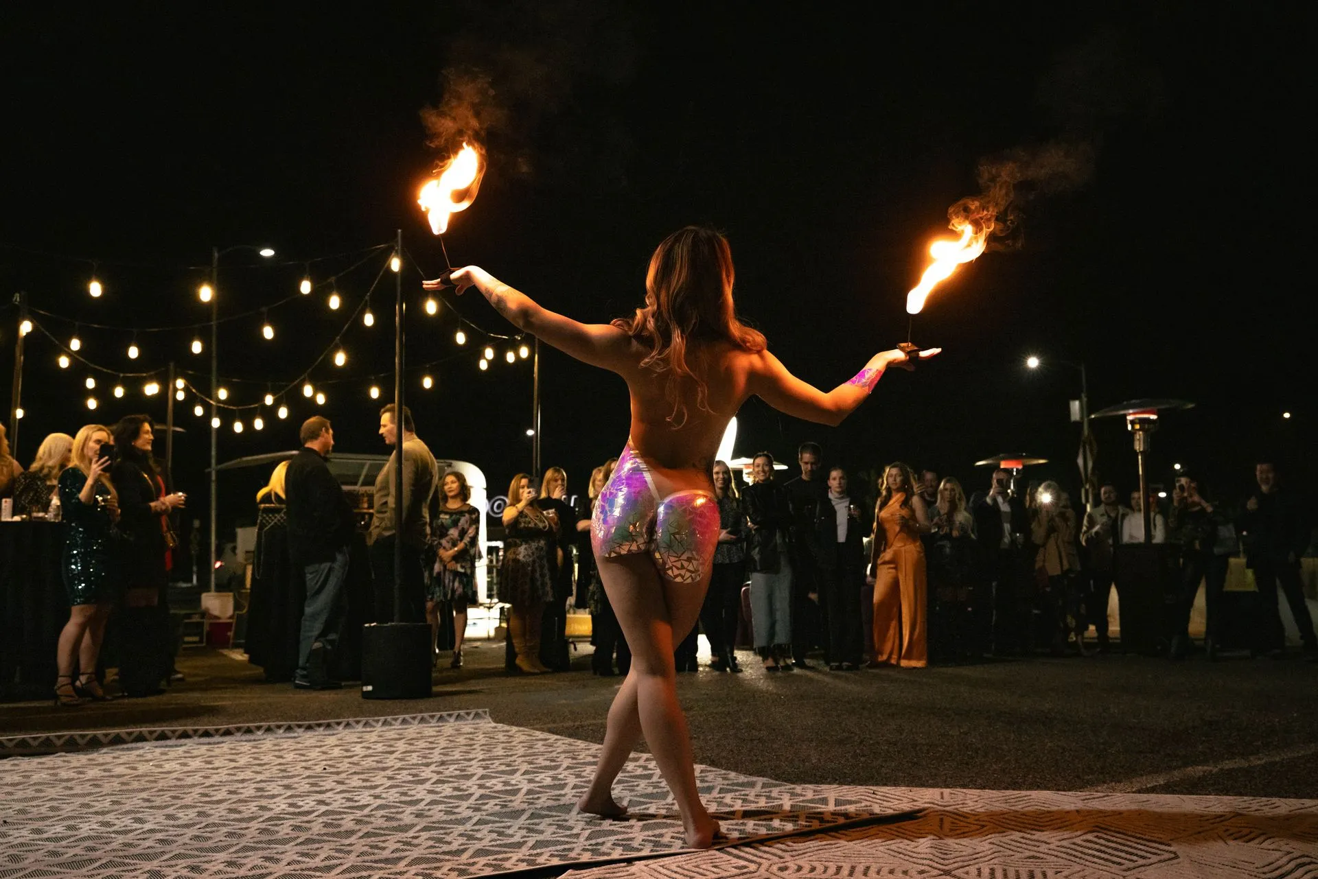 A woman is holding two fire torches in her hands while dancing on the beach at night.