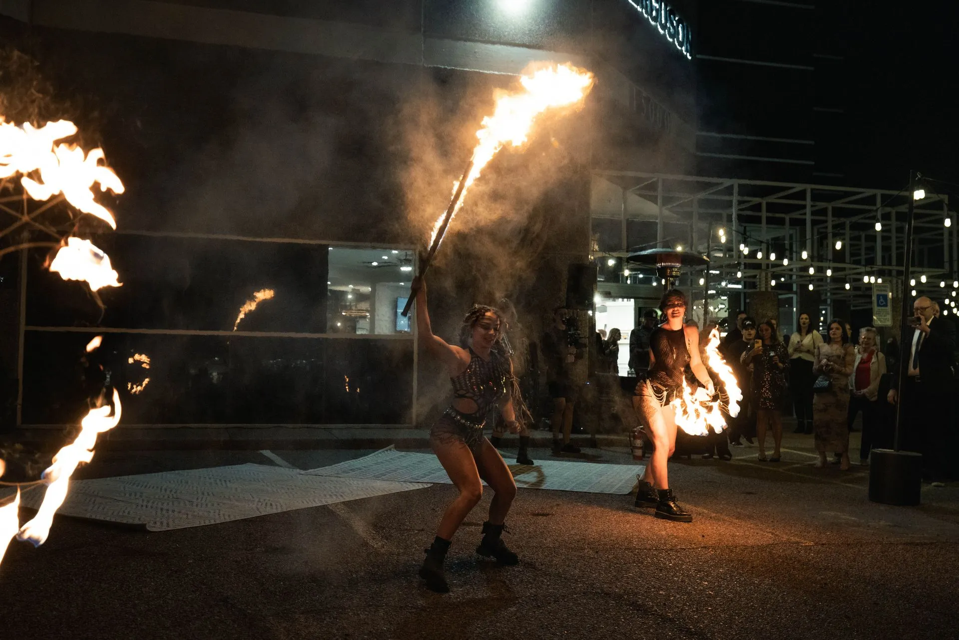 Two women are holding flaming torches in front of a building at night.