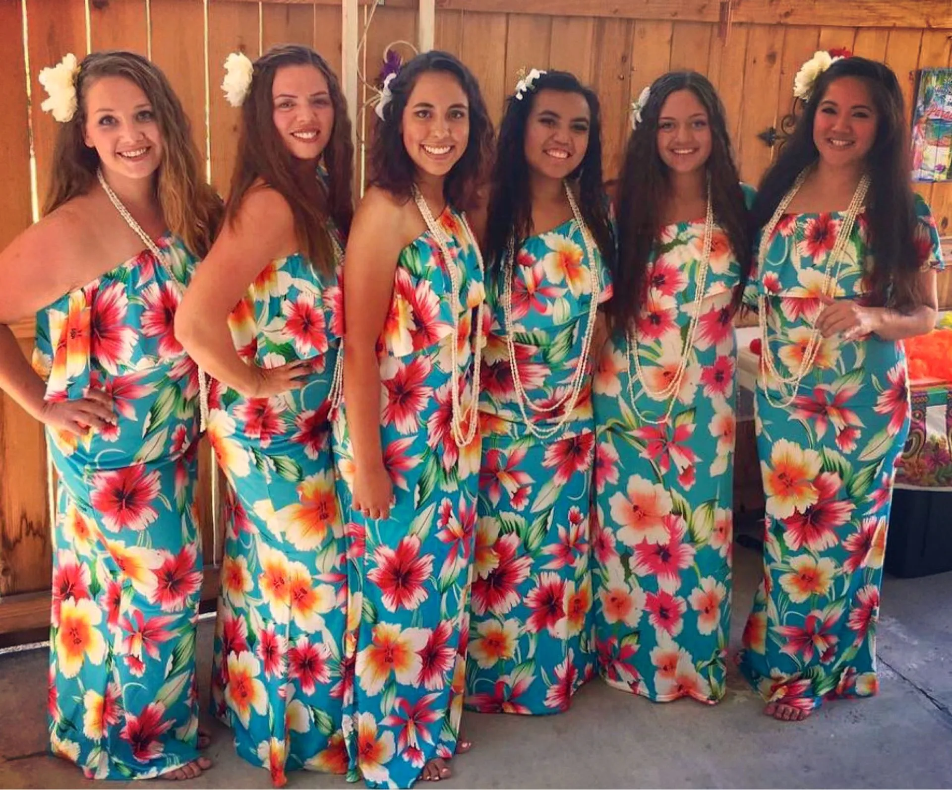 A group of women wearing hawaiian dresses are posing for a picture