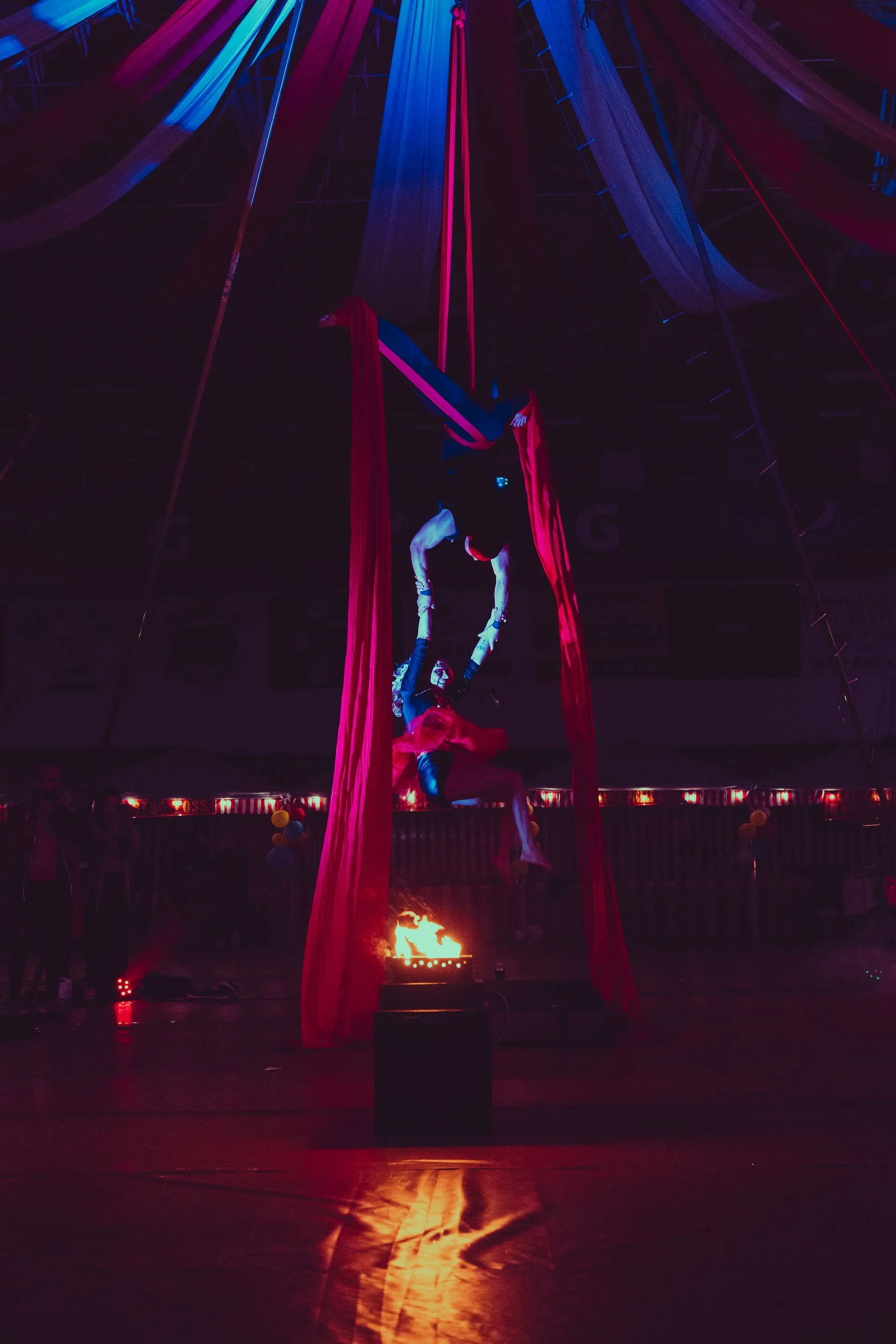 A woman is performing aerial acrobatics in a circus tent at night.