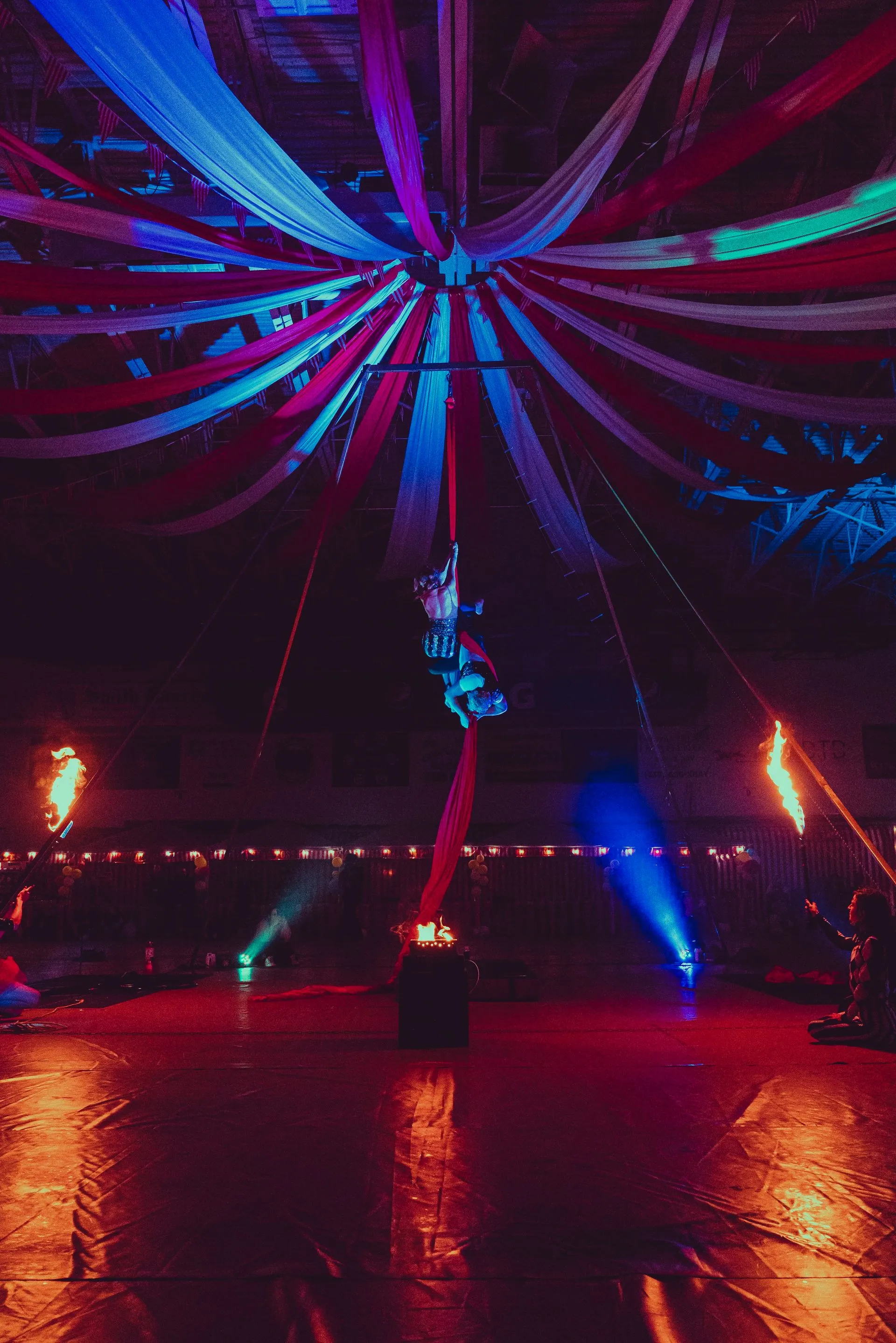 A man is flying through the air in a circus tent at night.