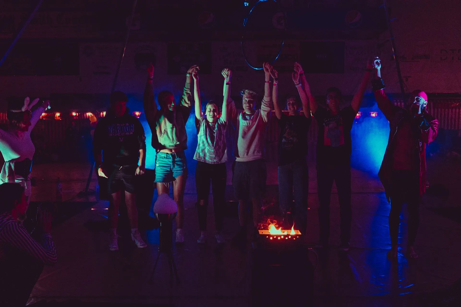 A group of people are standing in a dark room with their hands in the air.