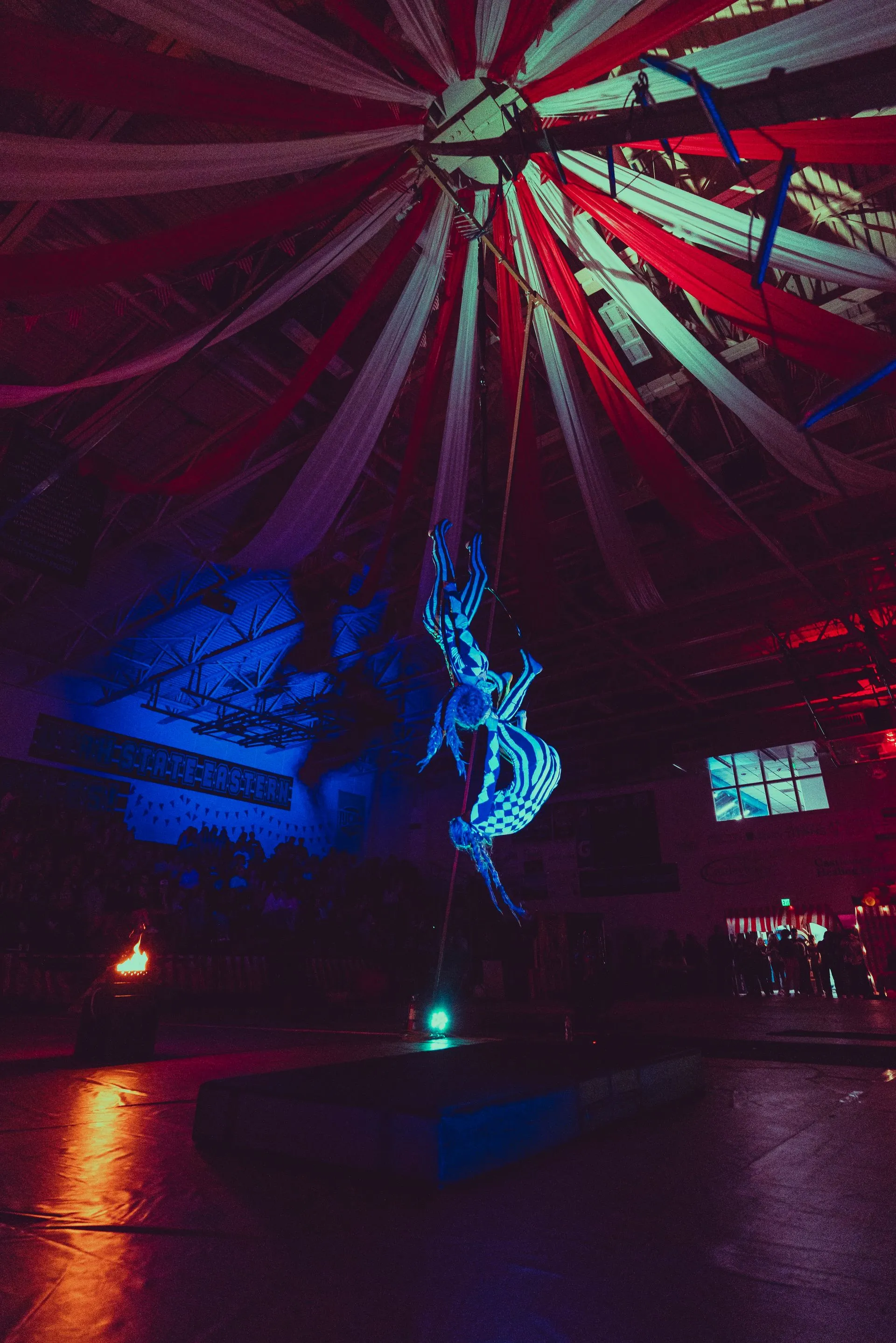 A person is hanging from a pole in a dark room with a colorful ceiling.