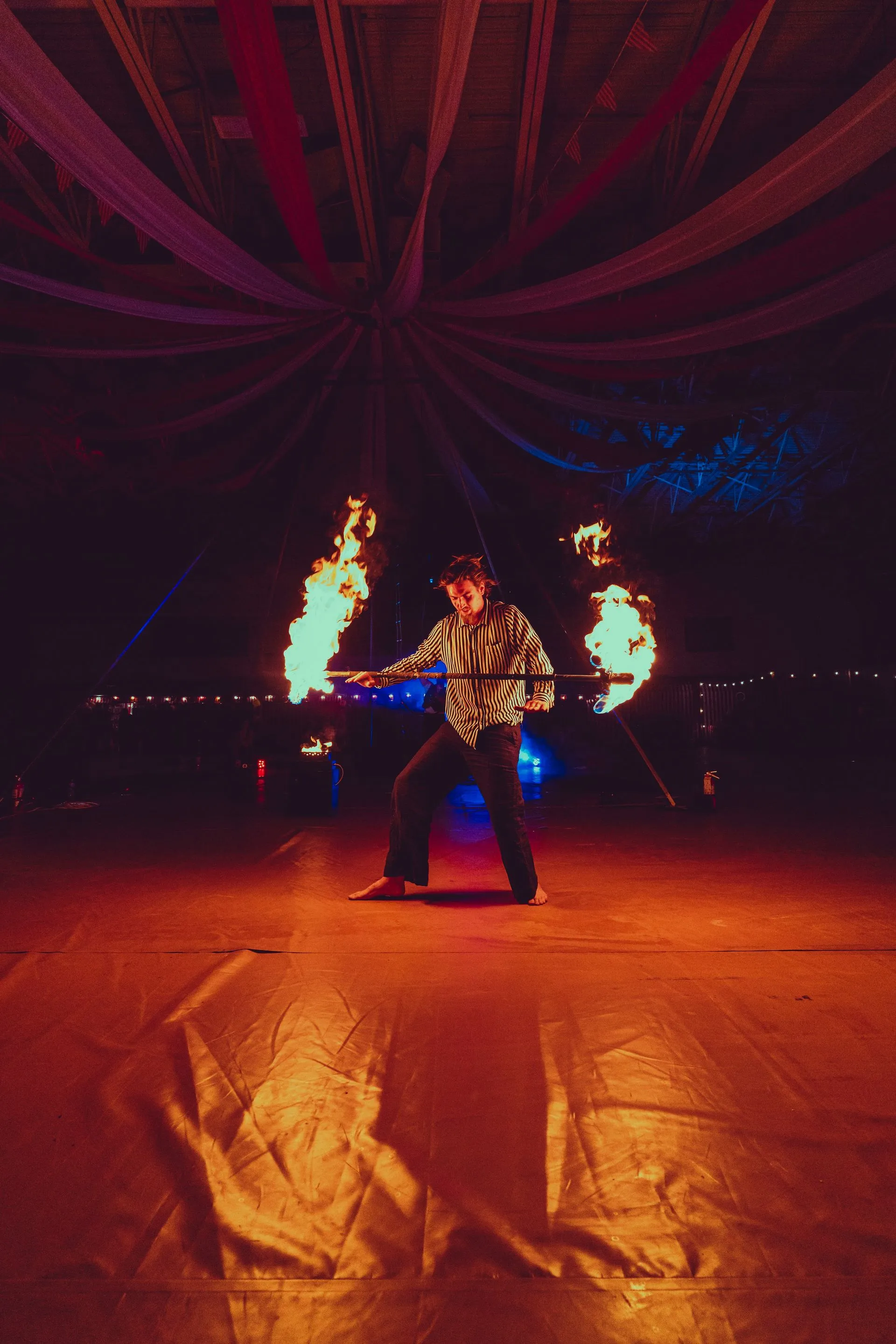 A man is holding two torches of fire in a dark room.