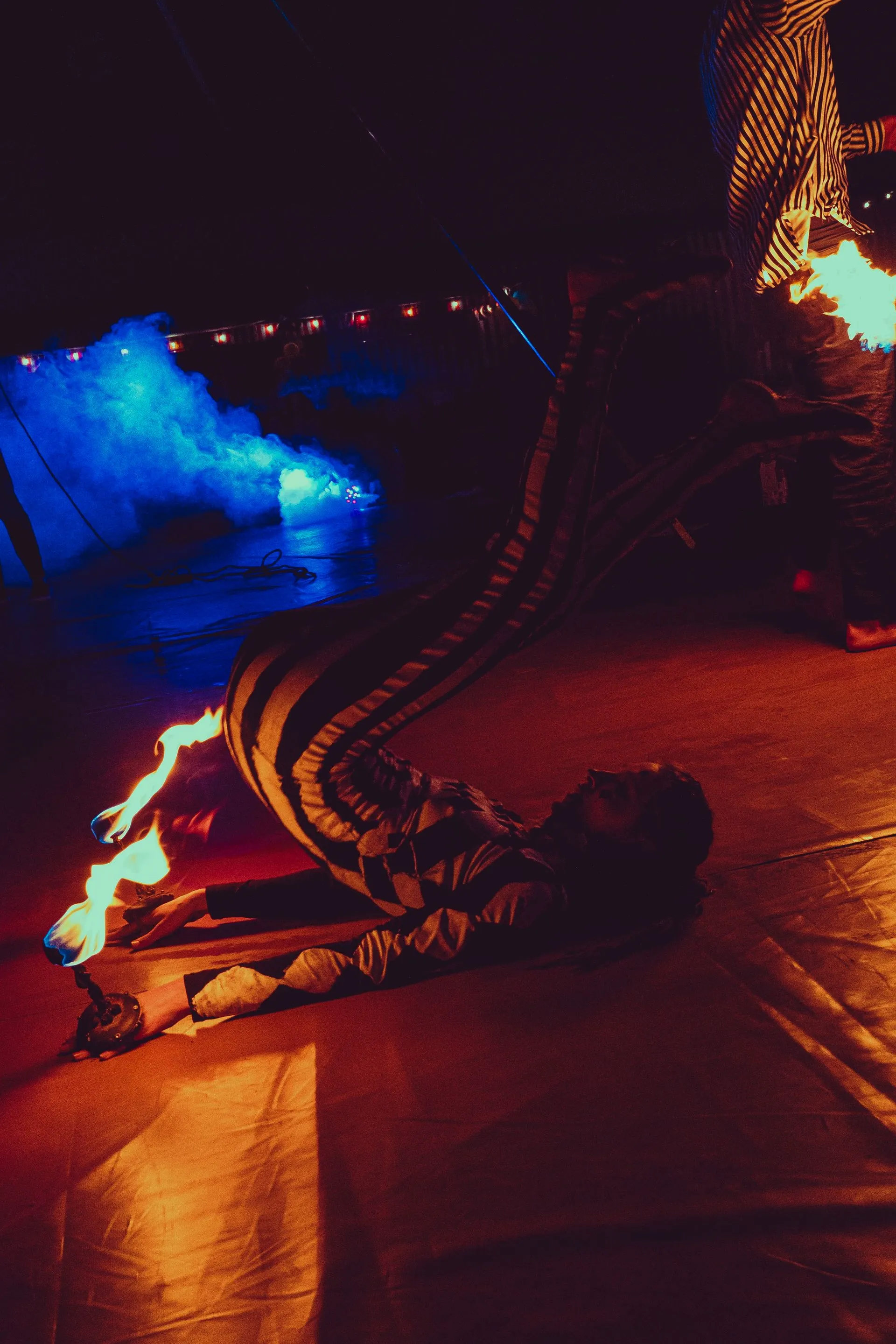A person is laying on the ground in front of a fire.