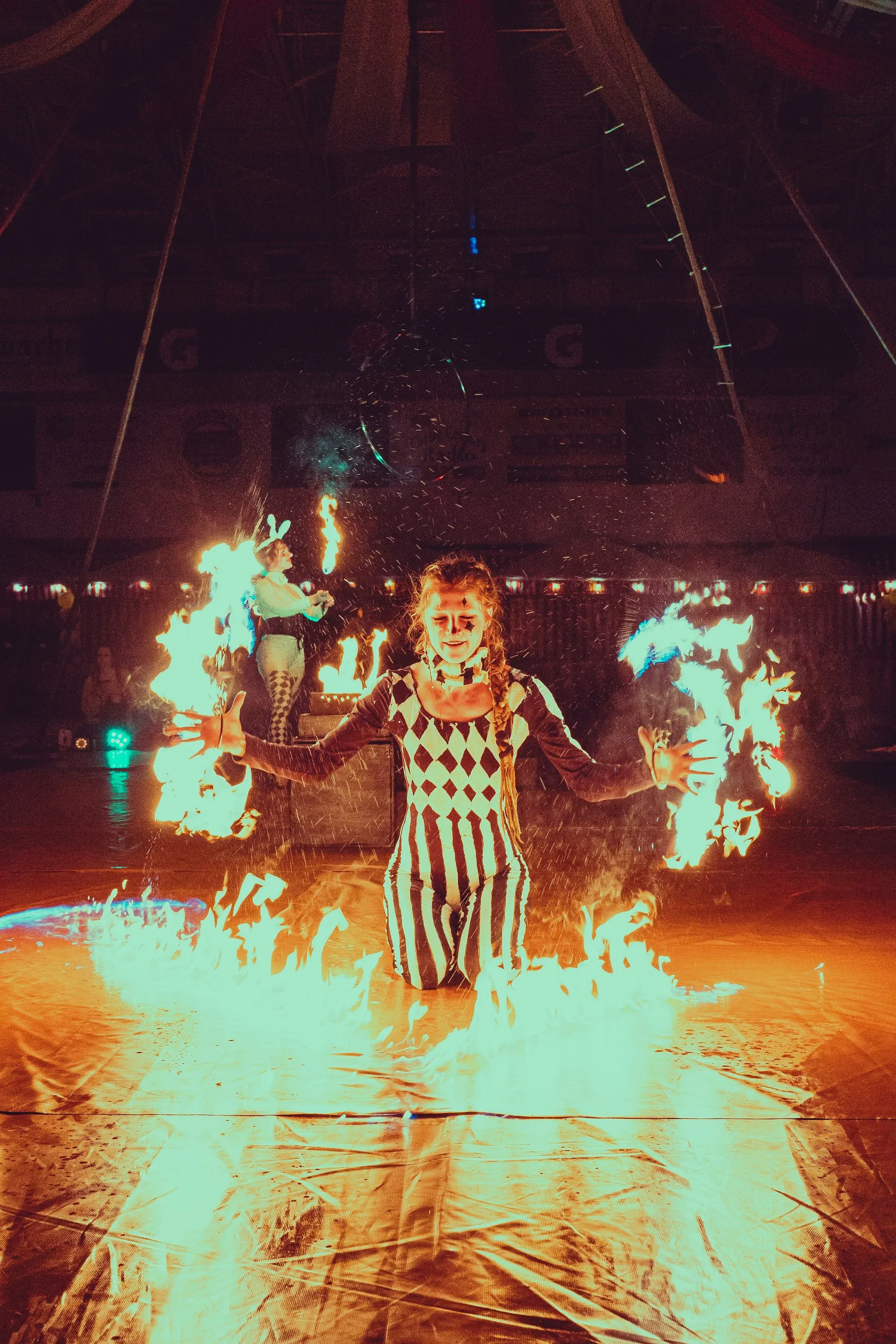 A woman performing with fire fans indoors with big fire on the ground.