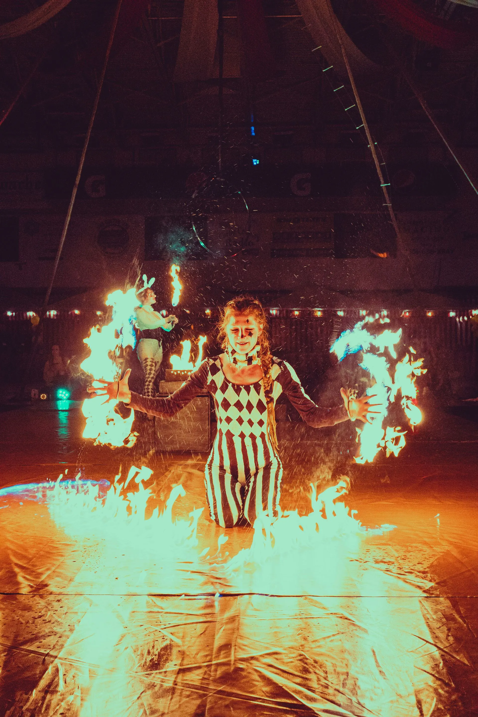 A woman performing with fire fans with big fire on the ground.