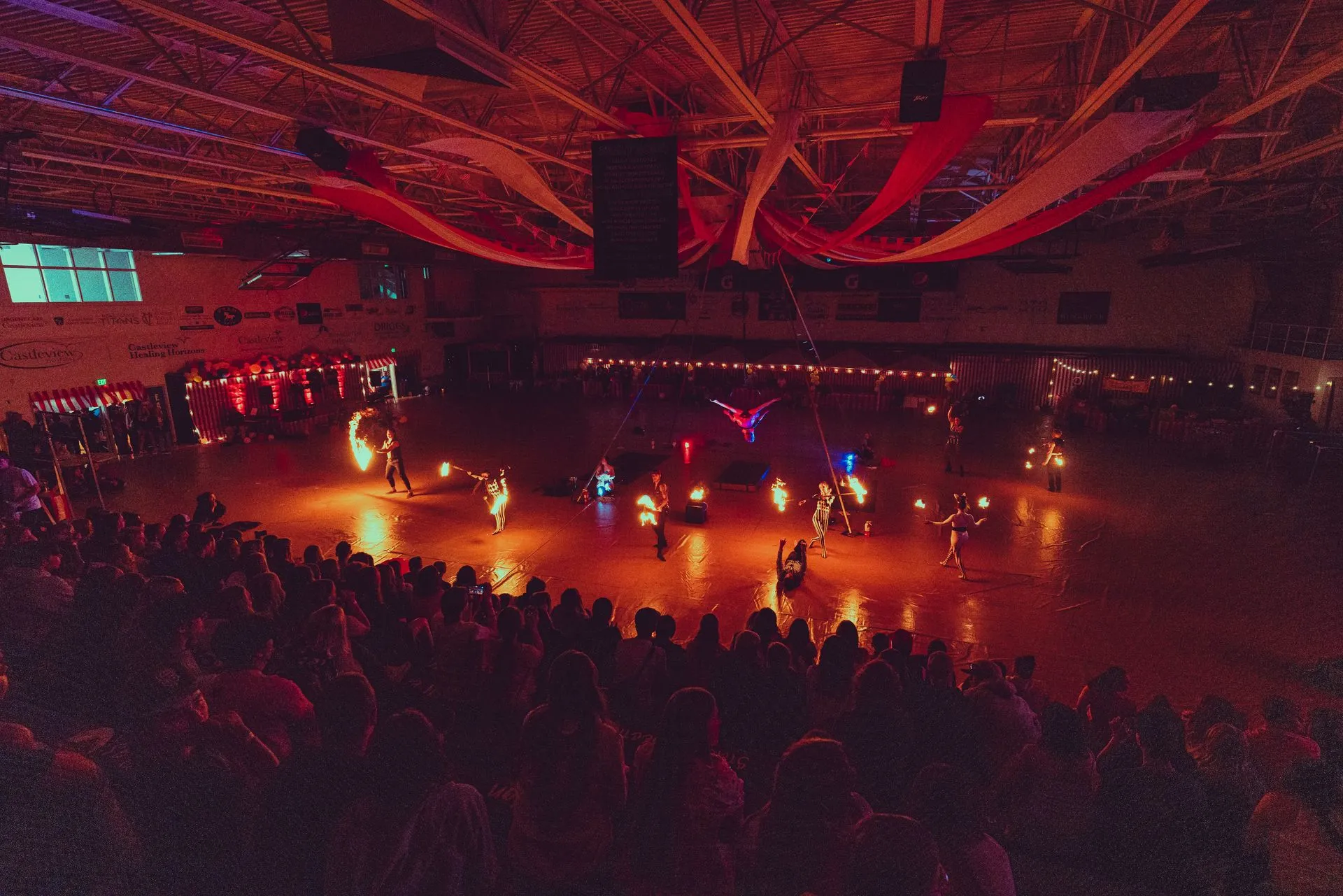 A crowd of people are watching a fire show in an indoor arena.