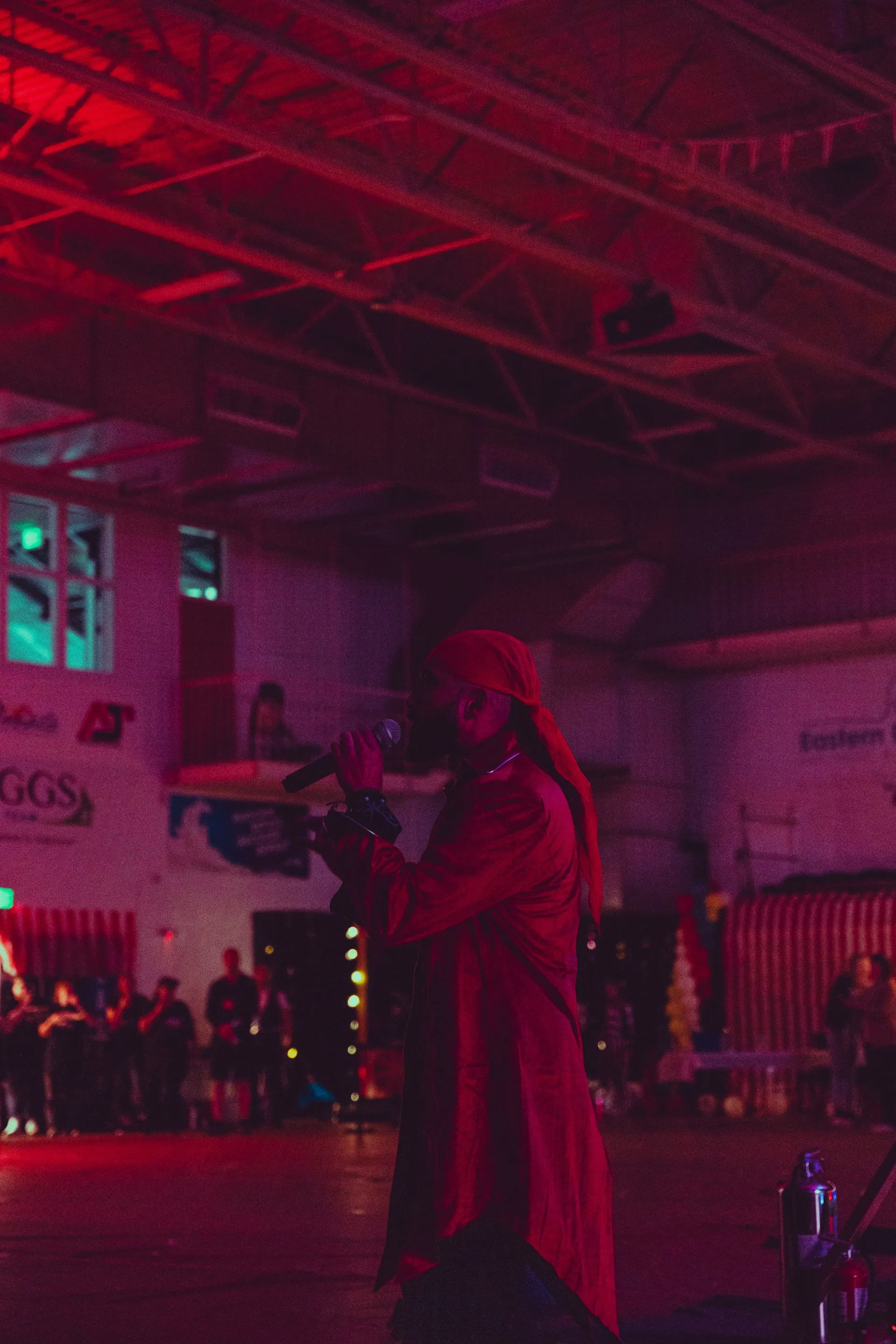A woman in a red dress is singing into a microphone in a dark room.