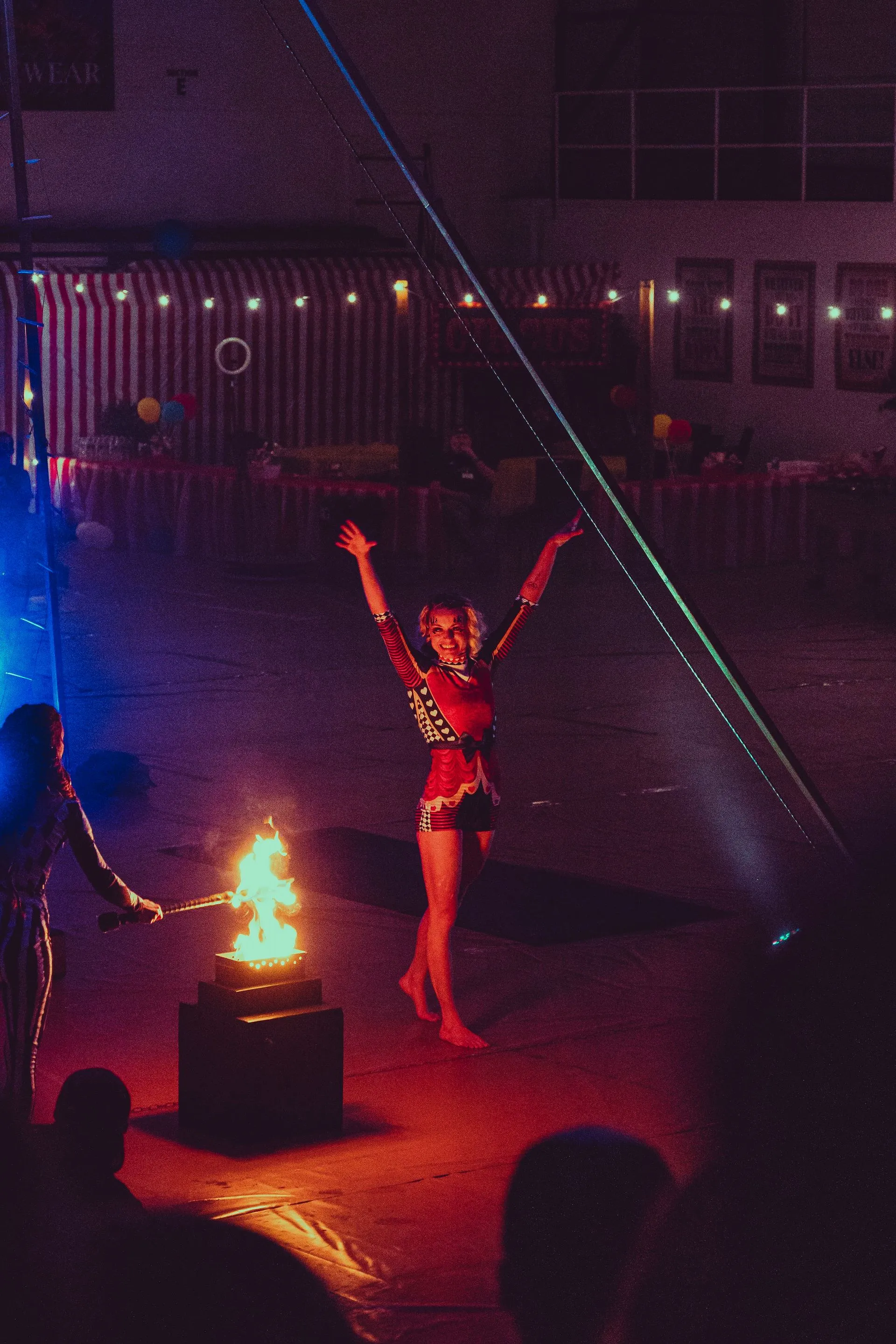 A woman is standing in front of a fire with her arms in the air