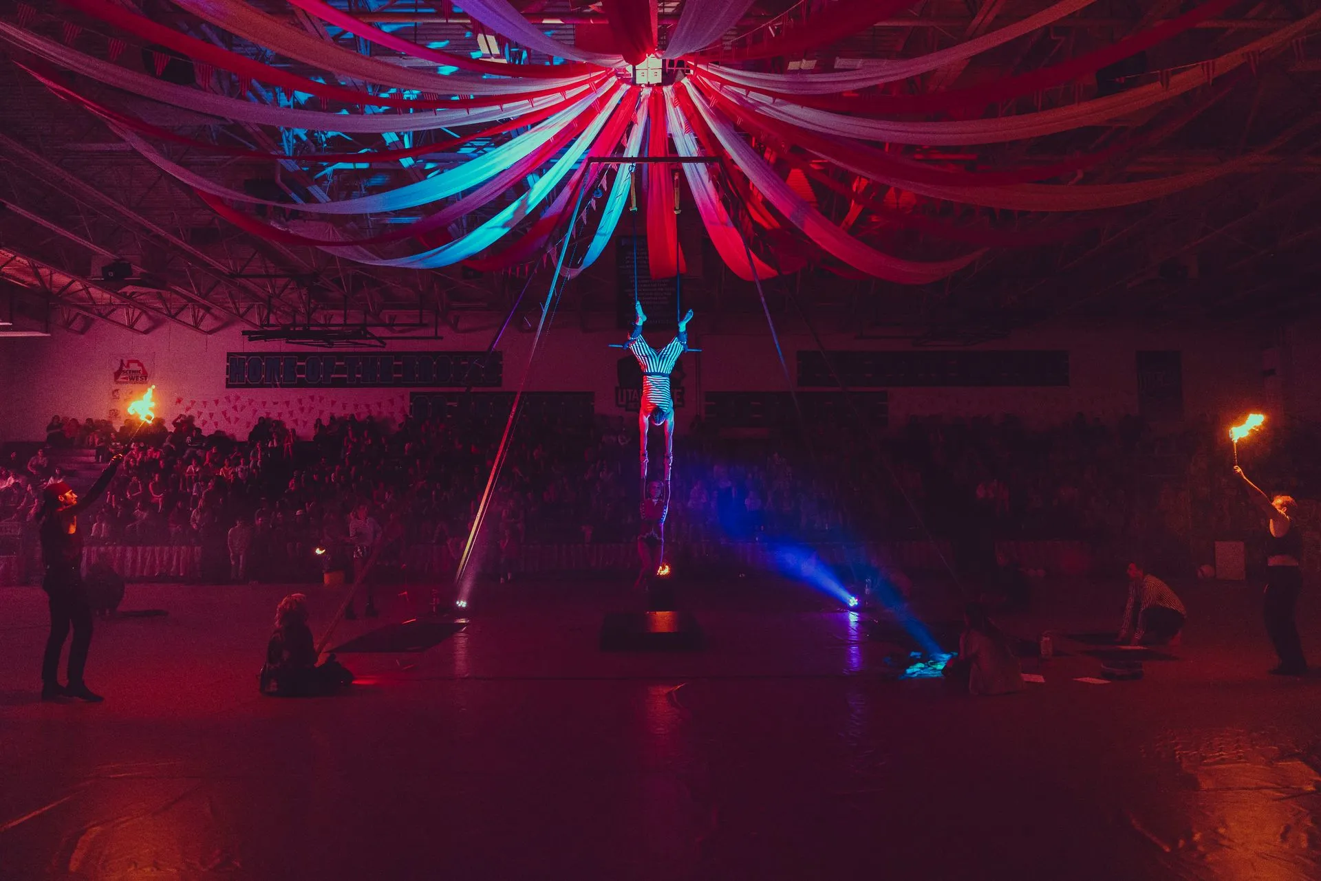 A person is standing on a pole in a dark room with red , blue and white ribbons hanging from the ceiling.