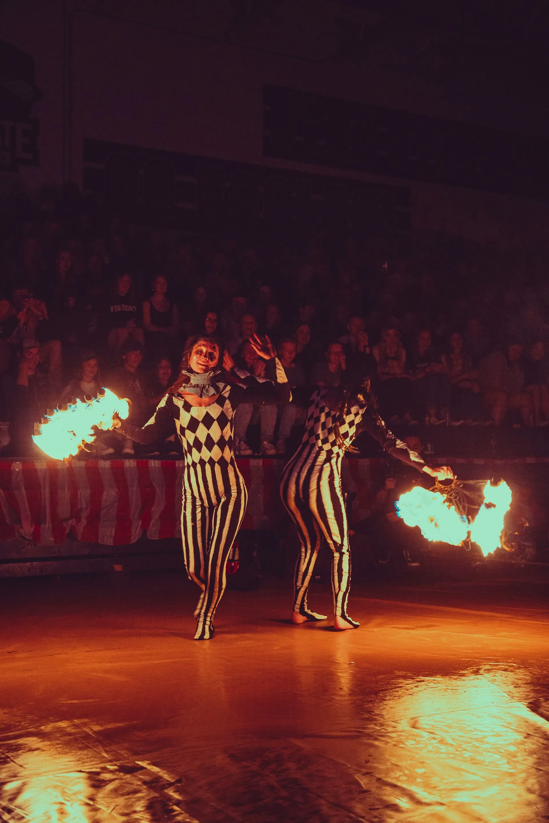 Two circus performers are holding fire in their hands in front of a crowd.