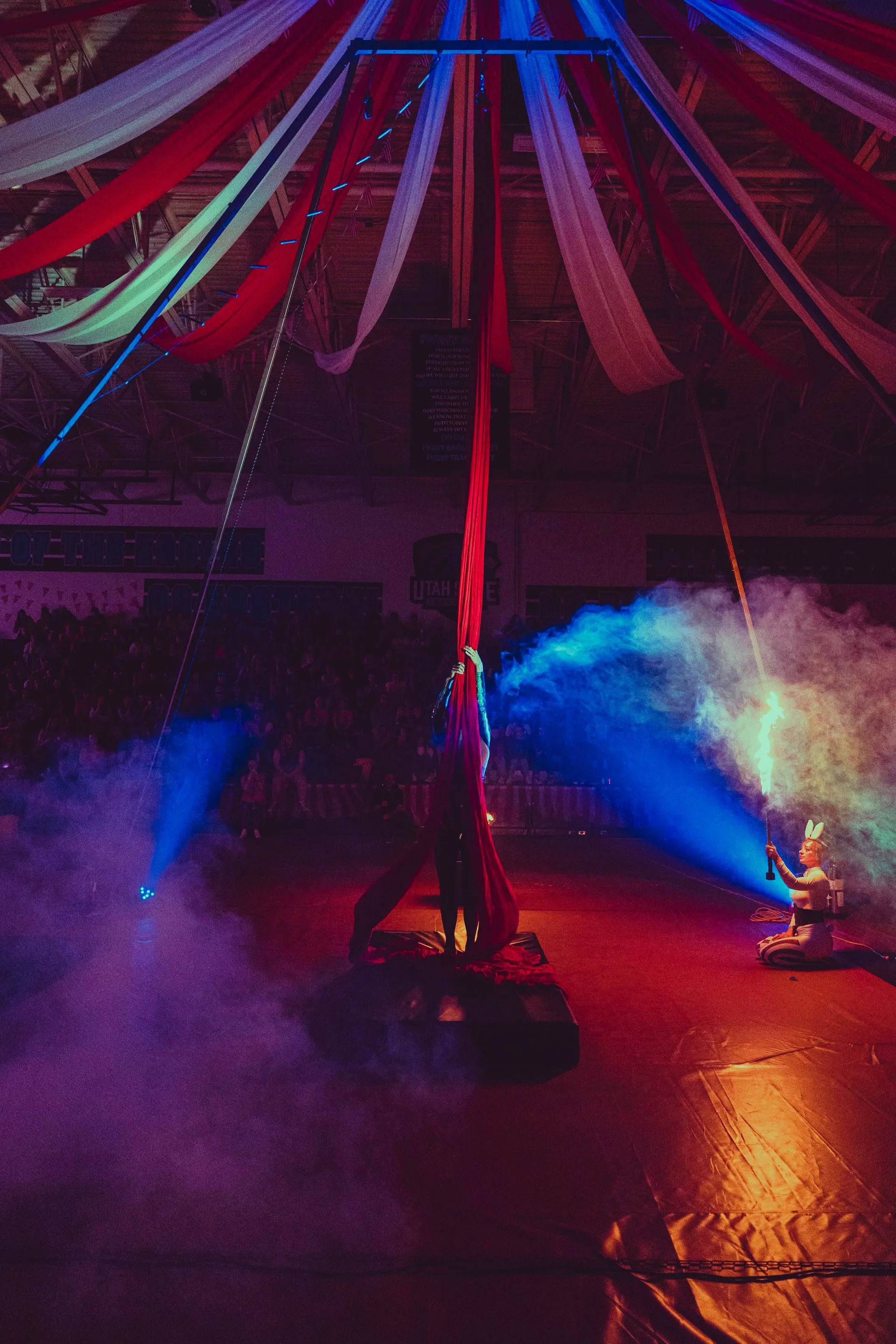 A woman is performing aerial acrobatics in a circus tent.