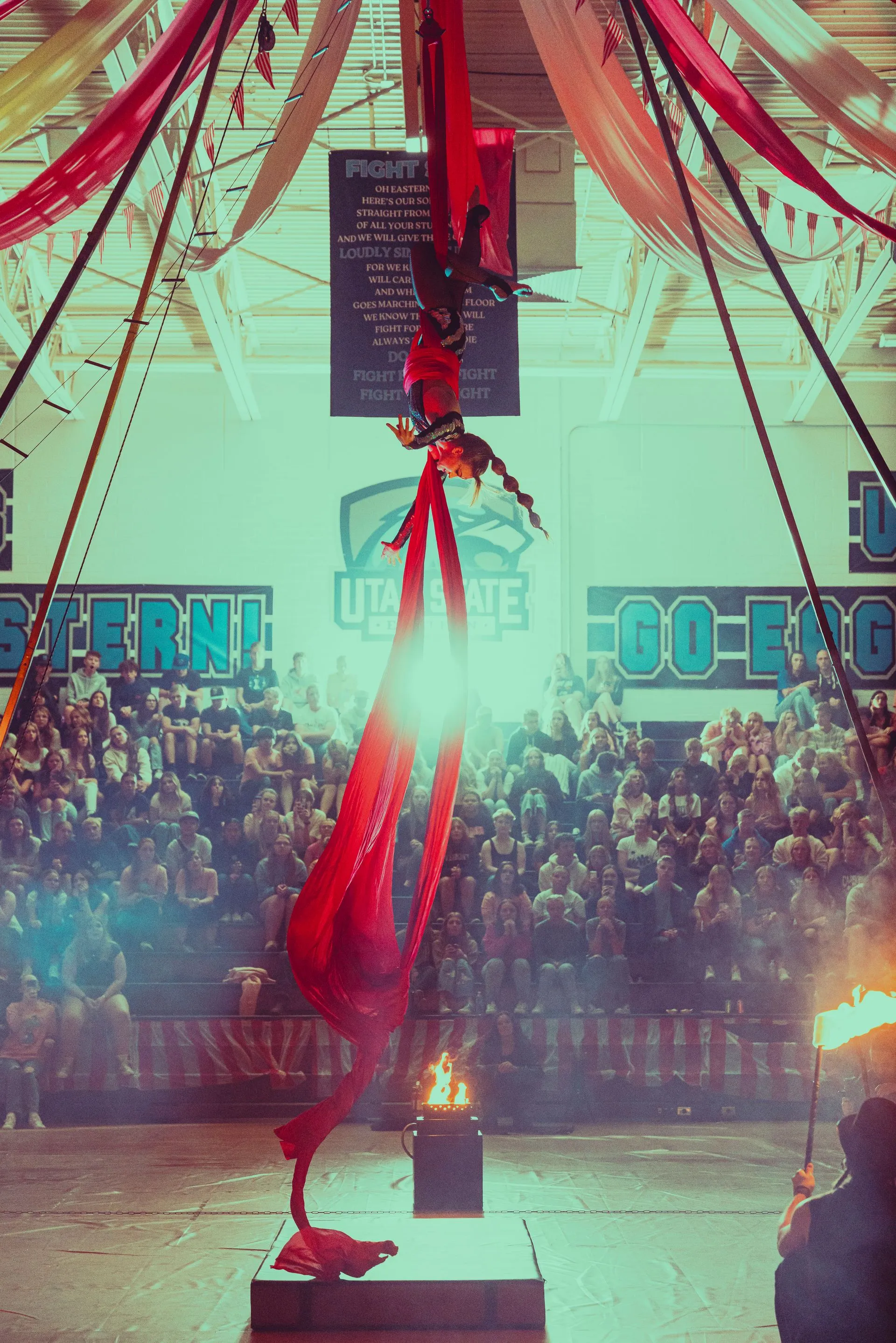 A person is performing aerial acrobatics in front of a crowd in a gym.