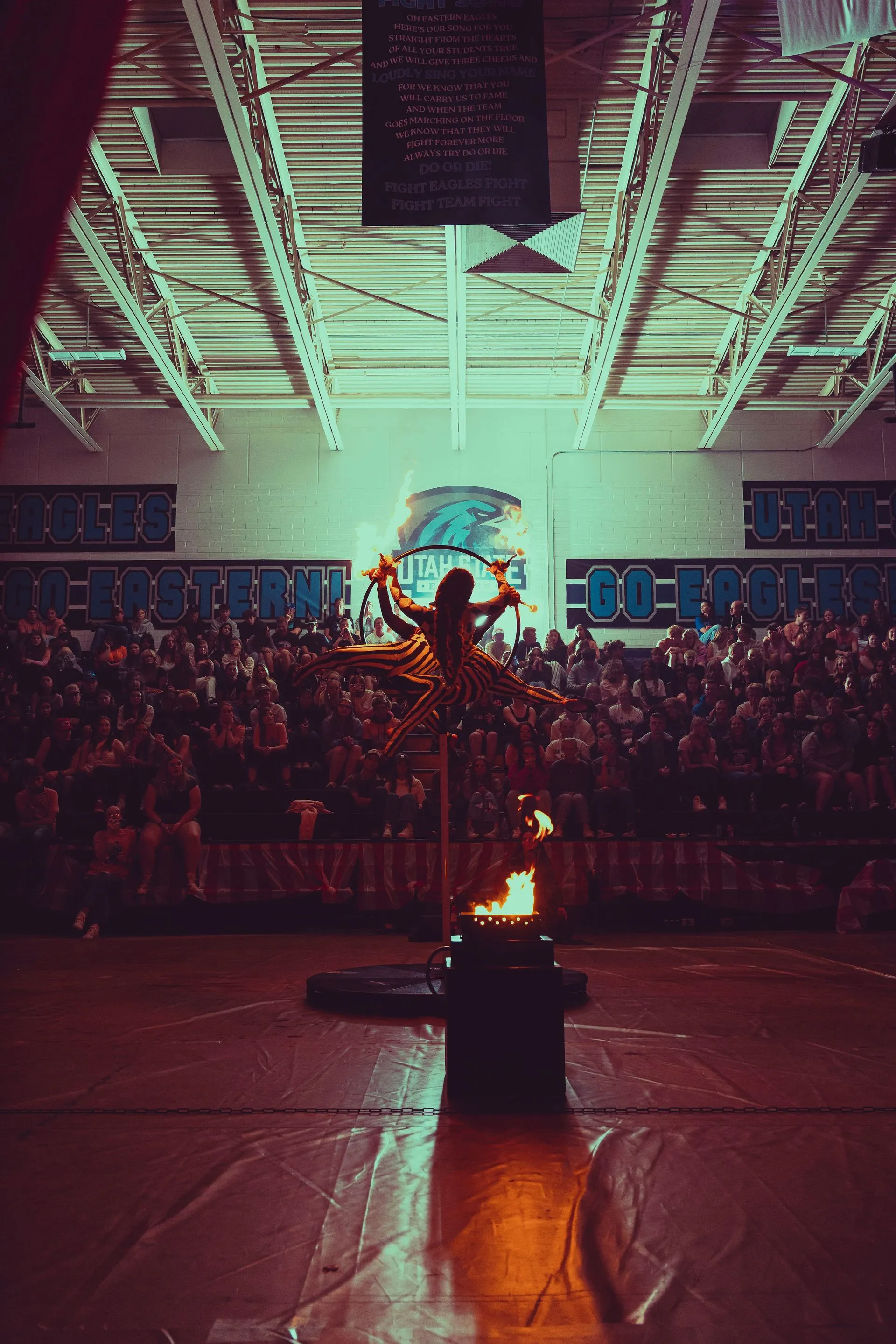 A woman is standing in front of a crowd in a gym holding a torch.