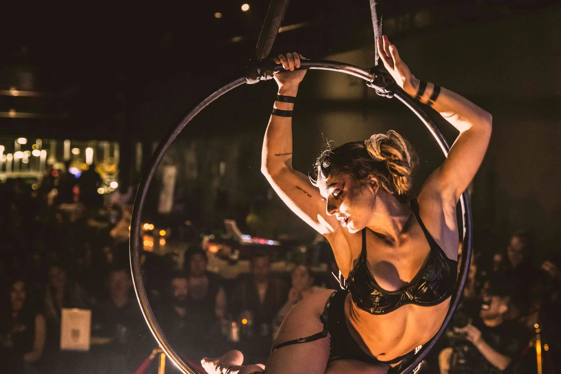 A woman is performing aerial acrobatics in a hoop in front of a crowd.