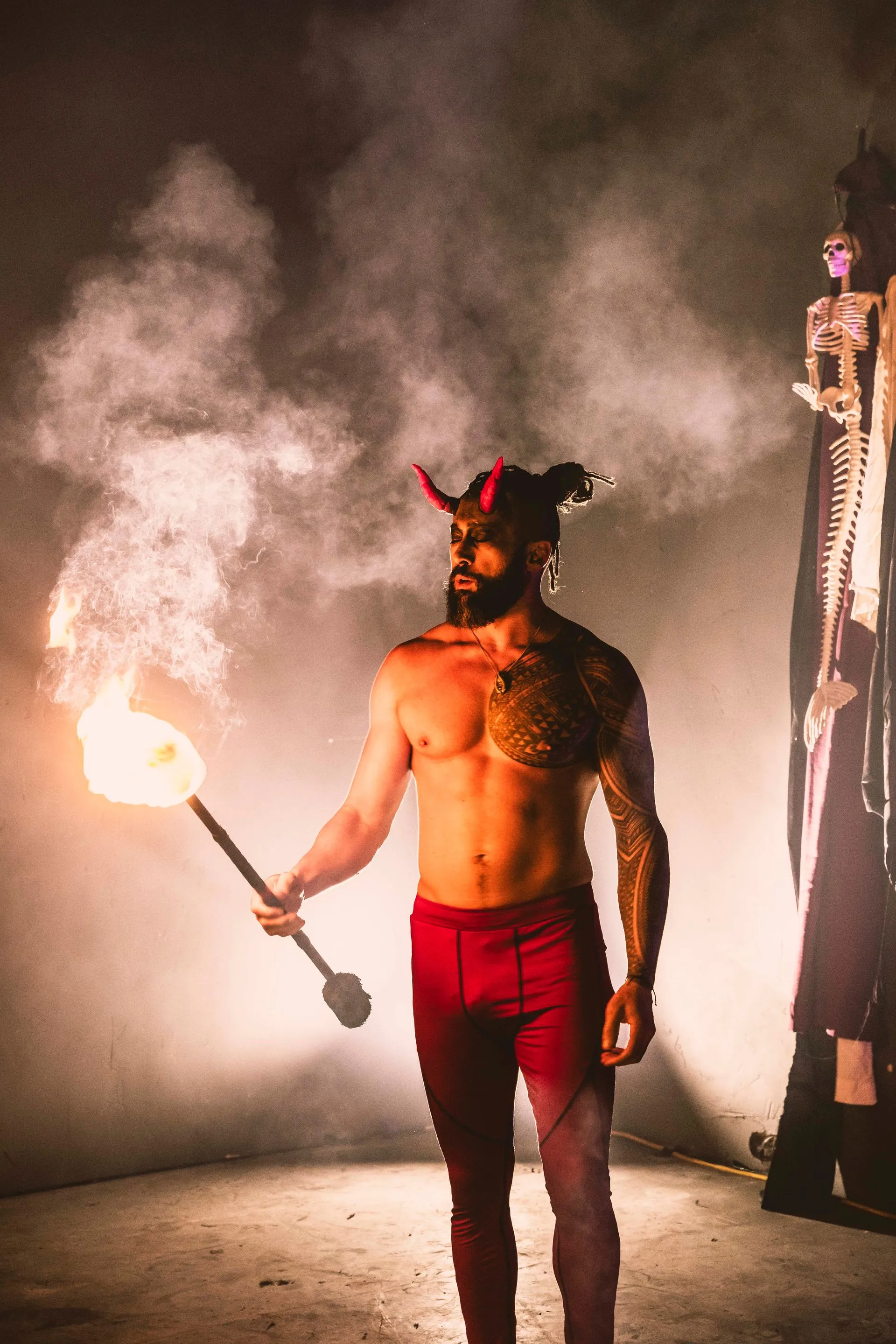 A shirtless man in a devil costume is holding a torch.