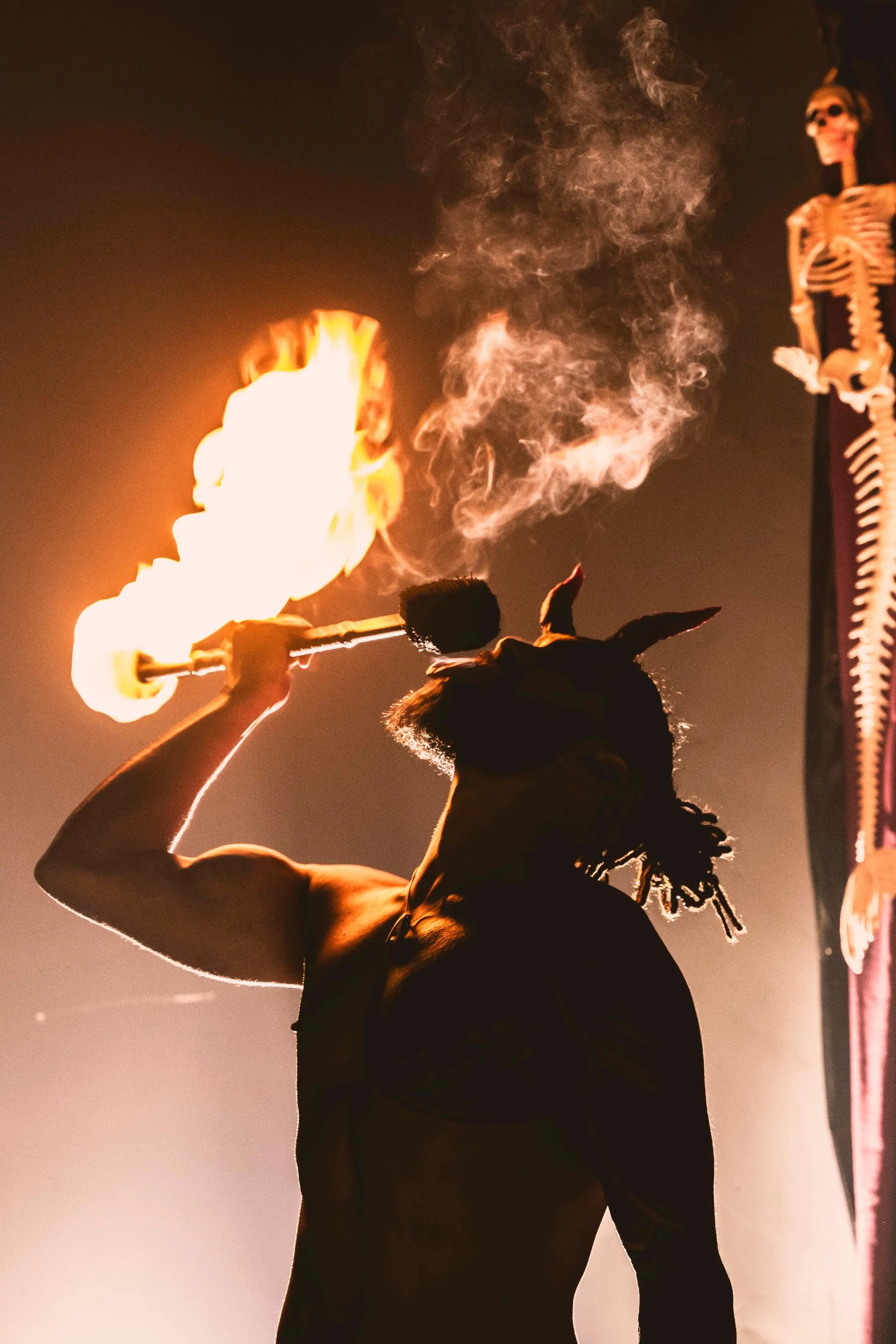 A man is blowing fire from a trumpet in front of a skeleton