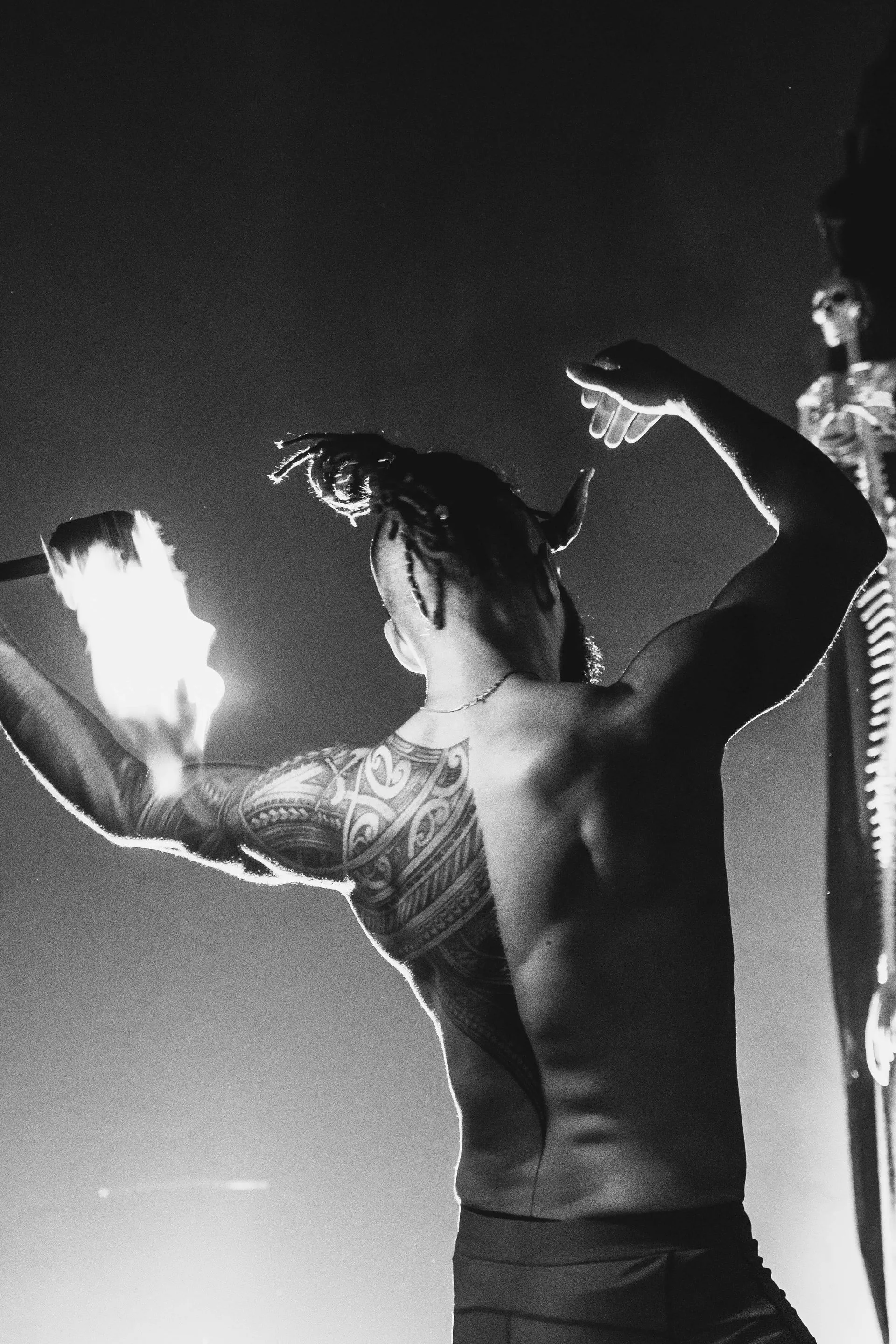 A black and white photo of a shirtless man holding a fire torch