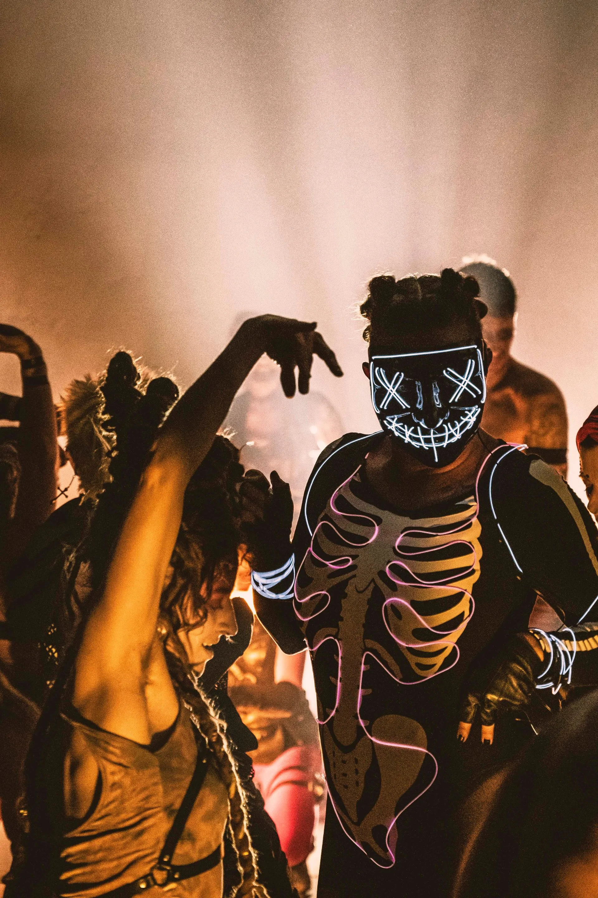 A woman in a skeleton costume is dancing with a man in a neon mask.